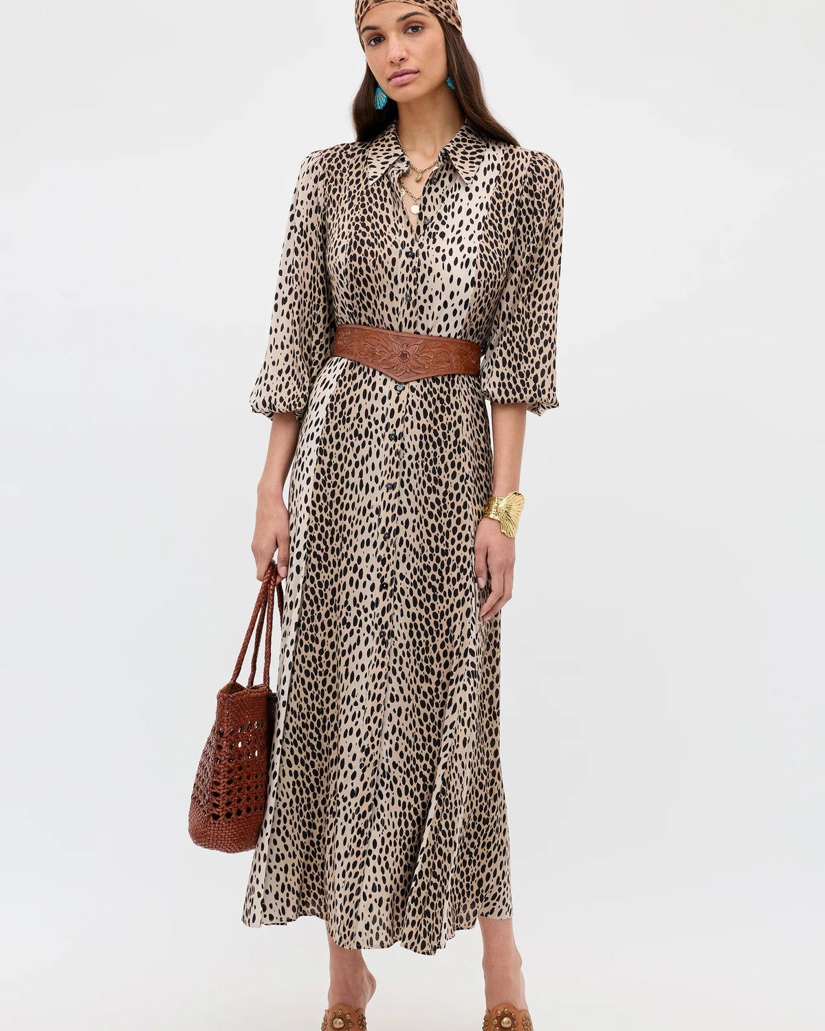 Woman wearing a leopard print dress with a brown belt and holding a brown bag on a white background