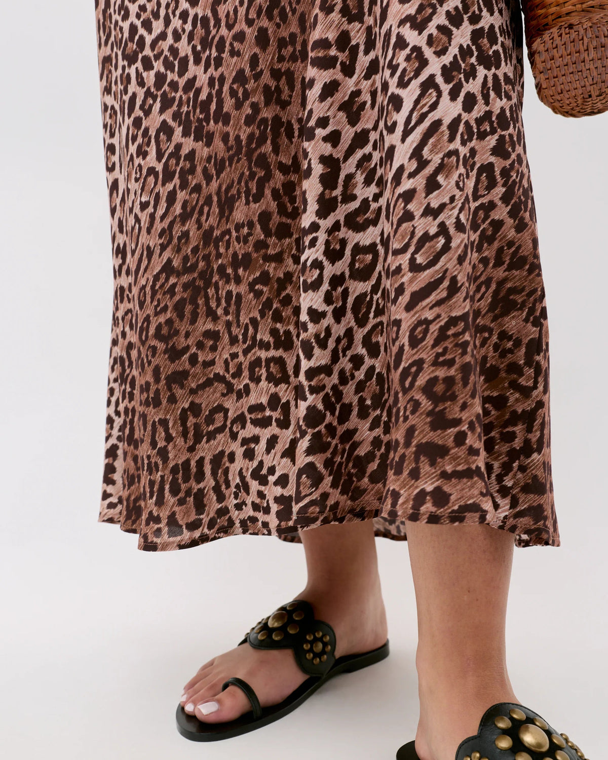 Person wearing a leopard print dress and black sandals on a white background