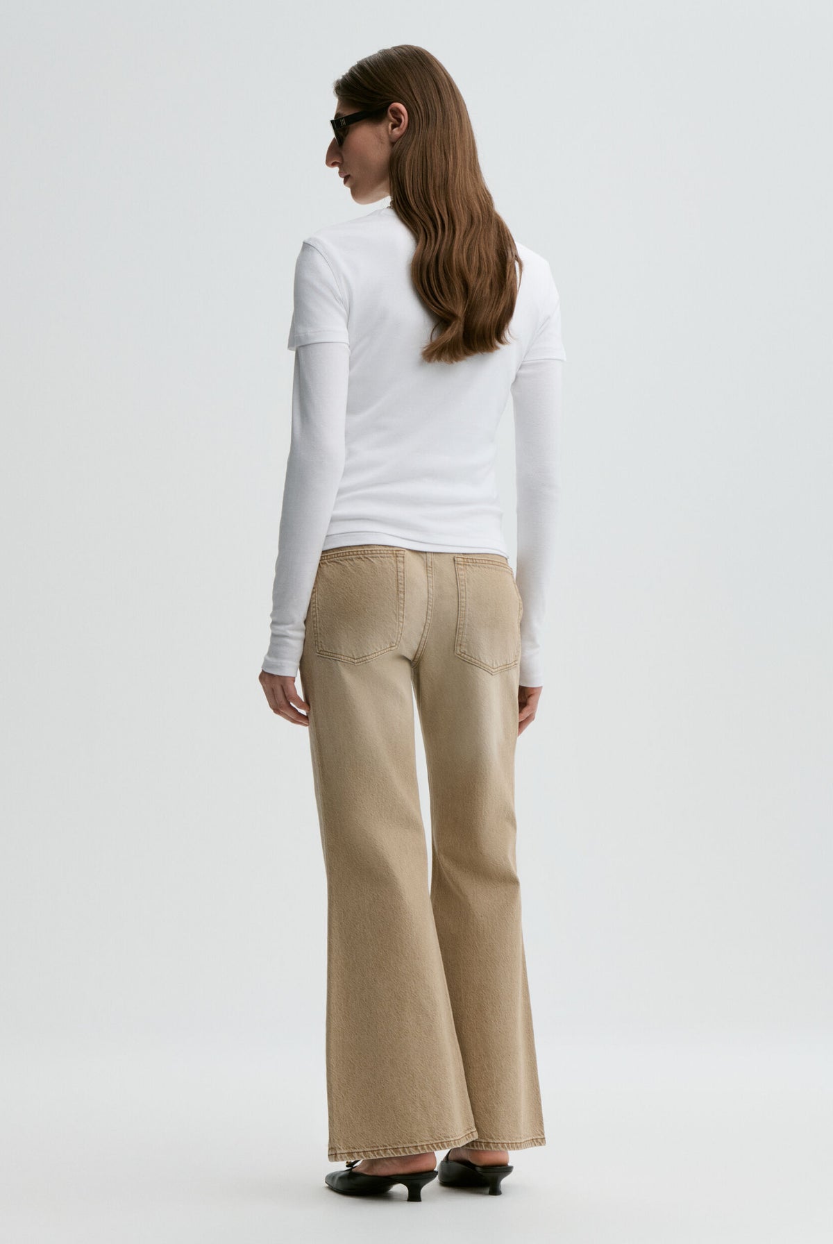 Woman wearing a white long-sleeve top and beige flared pants on a white background