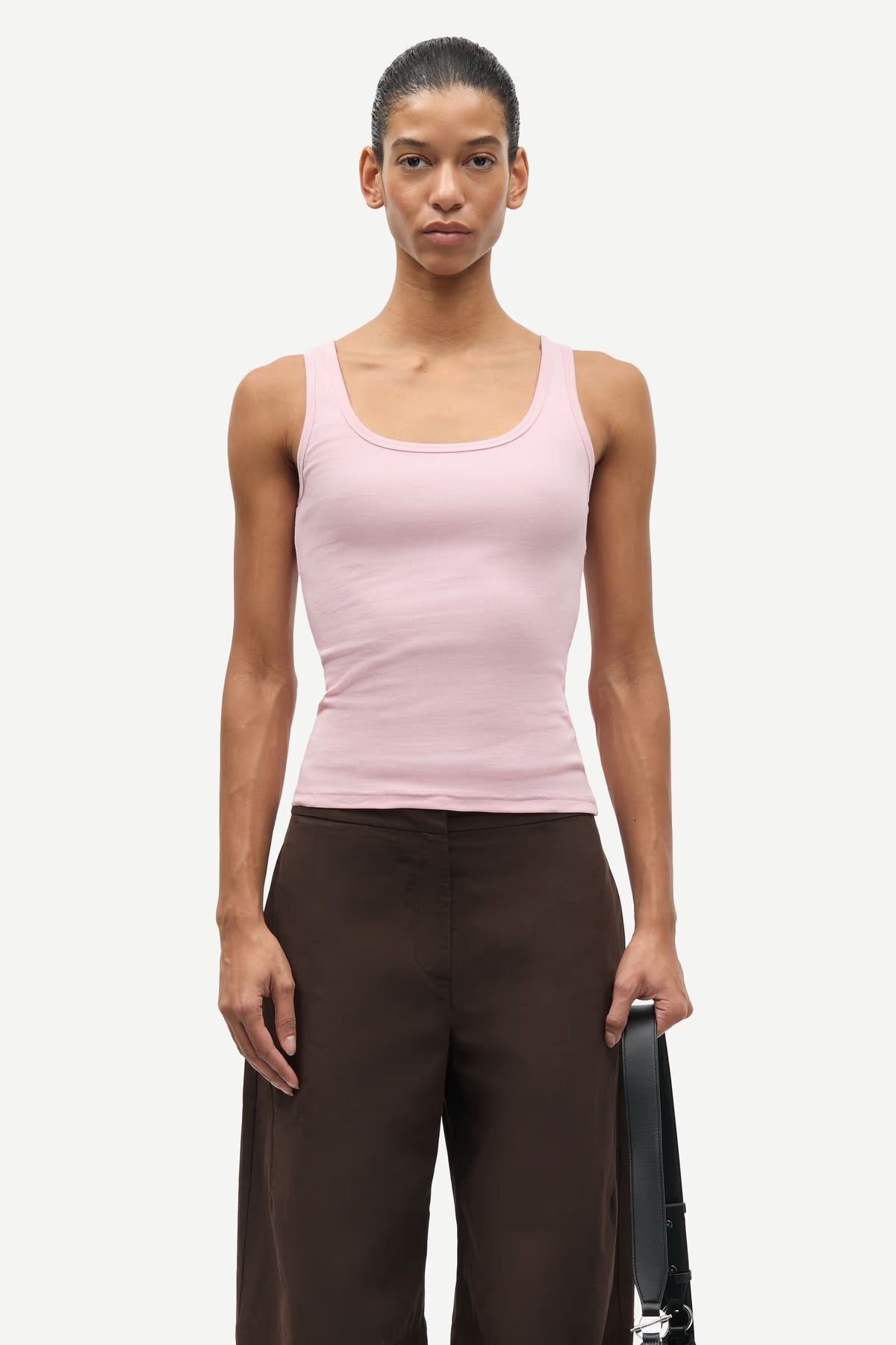 Person wearing a pink tank top and brown pants holding a black bag on a white background