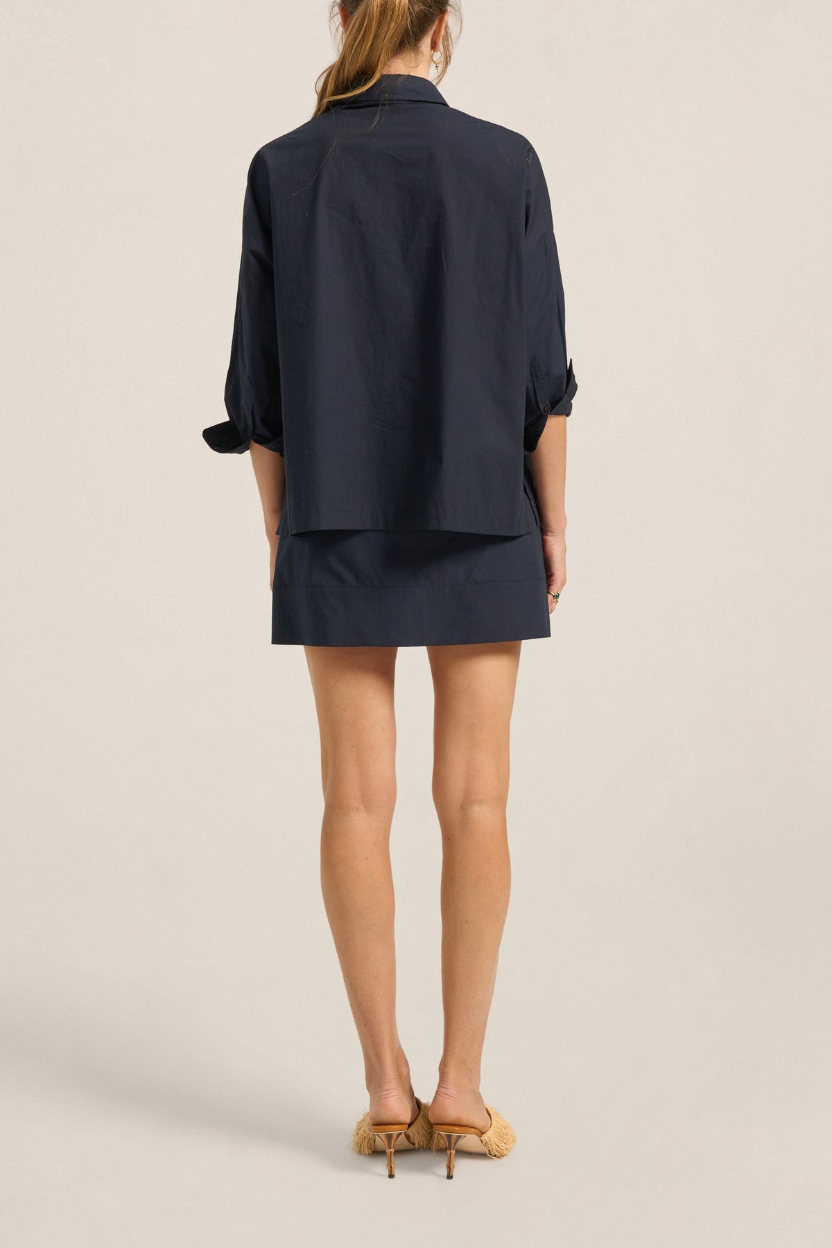 Person wearing a navy blue outfit with a jacket and skirt on a beige background