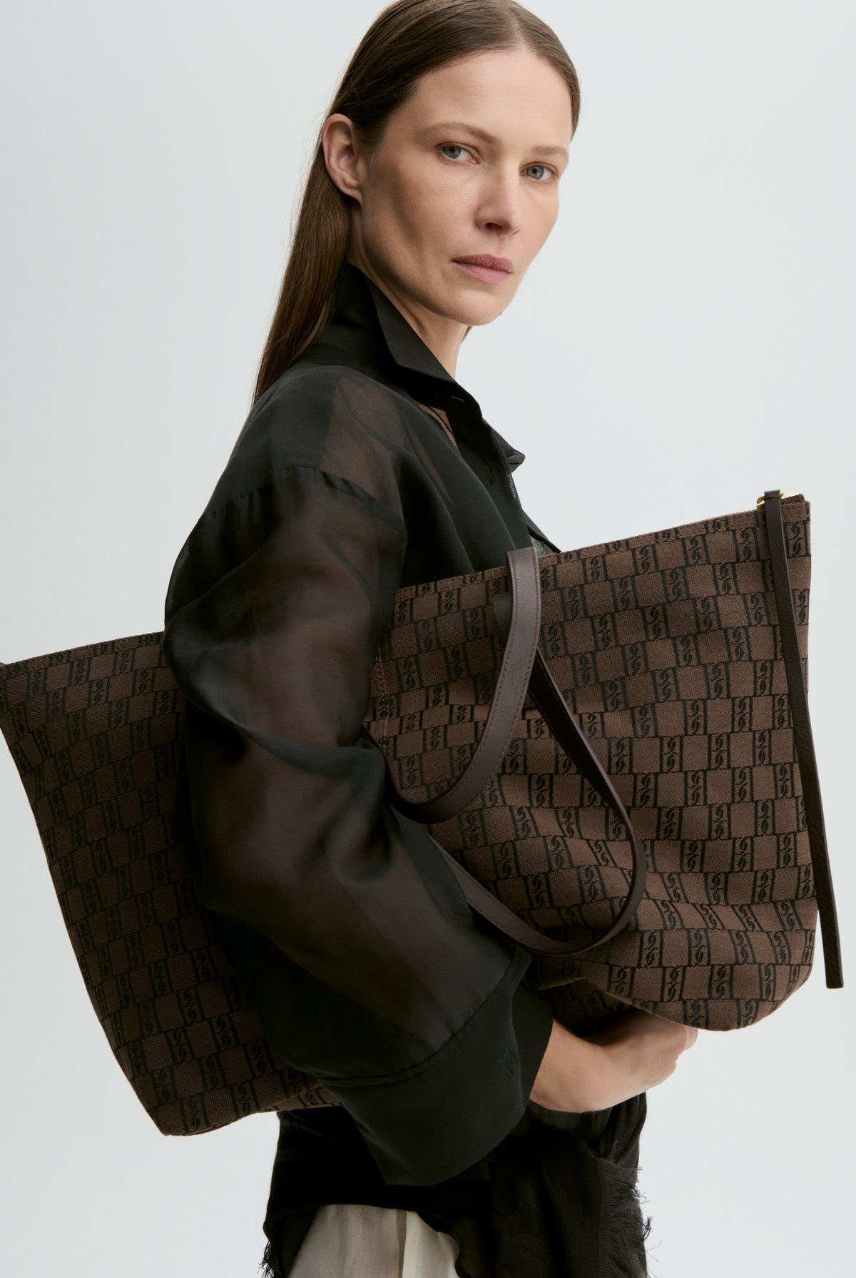 Woman holding a brown patterned bag against a light gray background