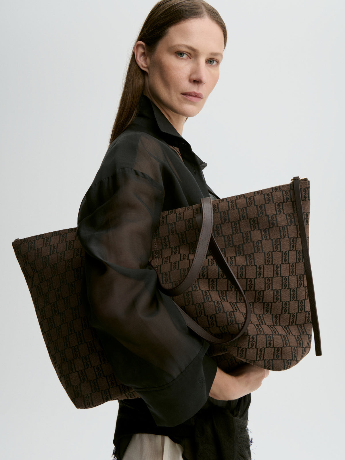 Woman holding a brown patterned bag against a light gray background