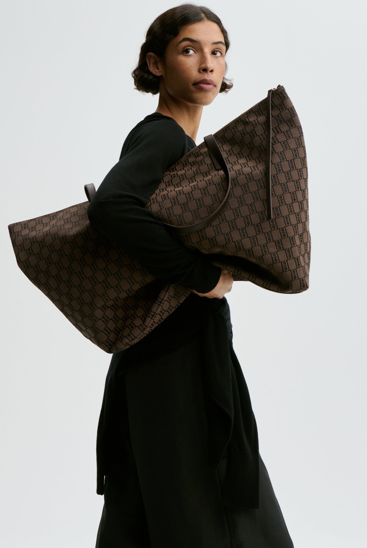 Person holding a large brown patterned bag against a plain background