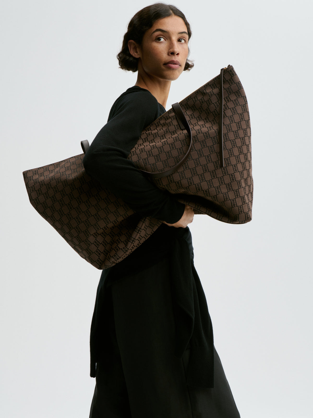 Person holding a large brown patterned bag against a plain background