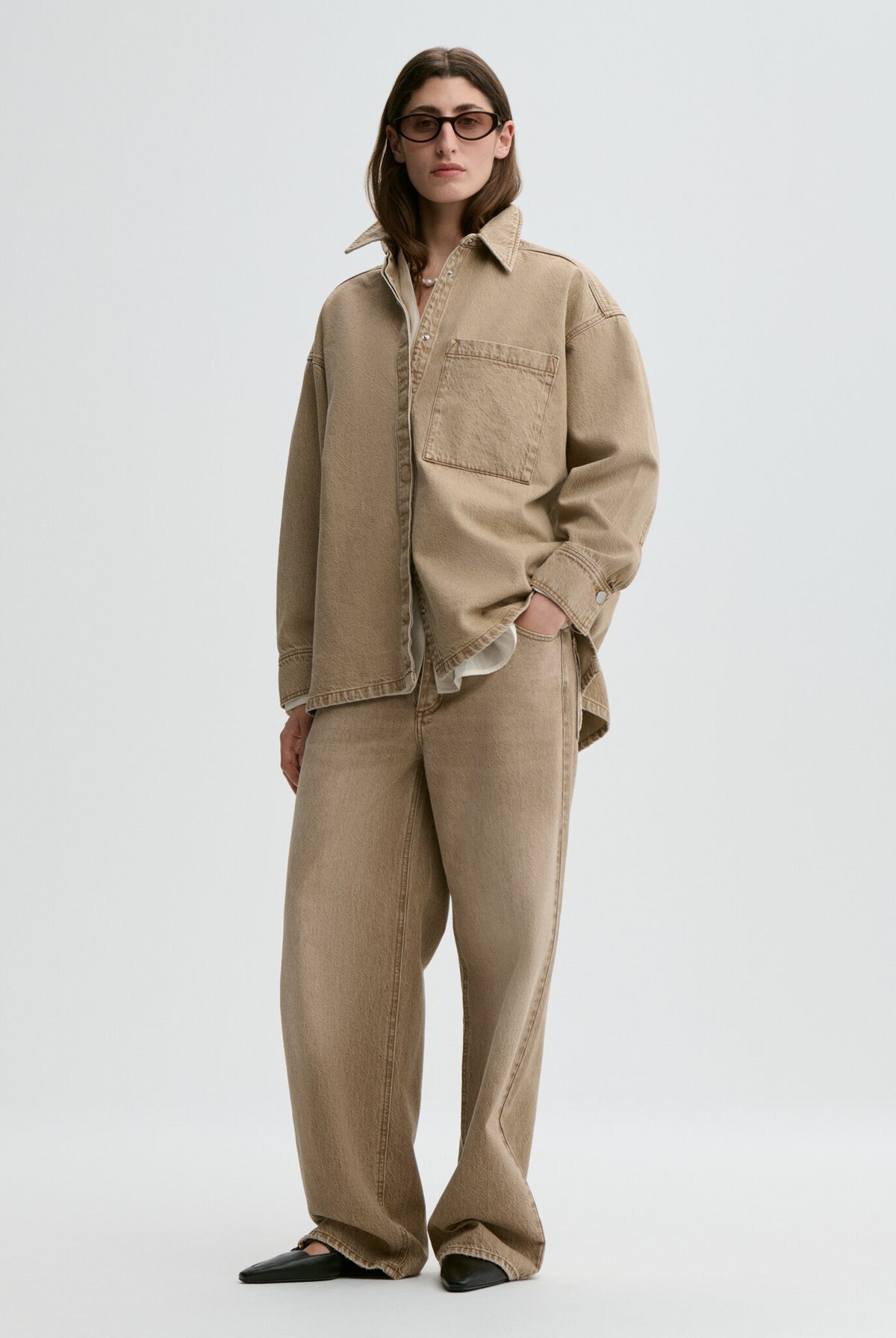 Person wearing a beige jacket and pants on a white background