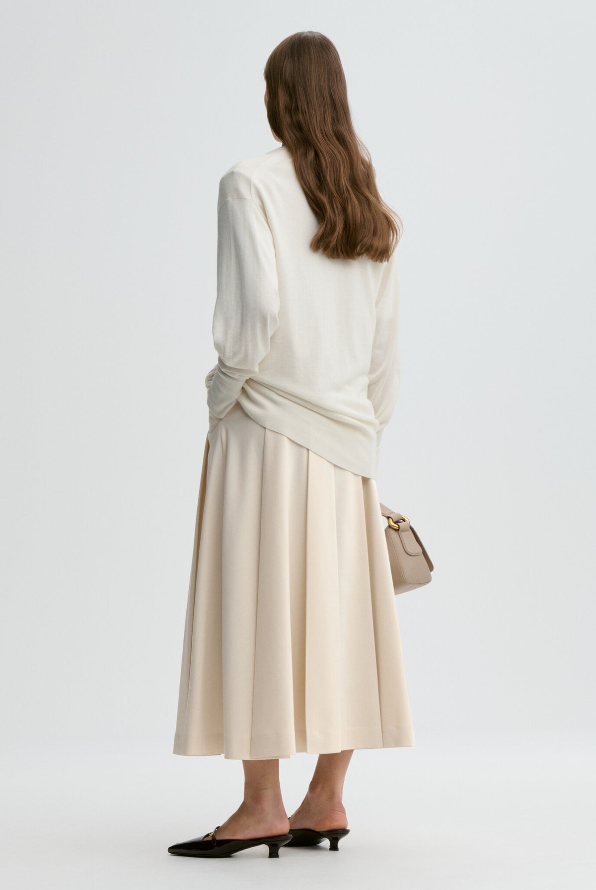 Woman wearing a white top and beige skirt with a handbag on a light gray background