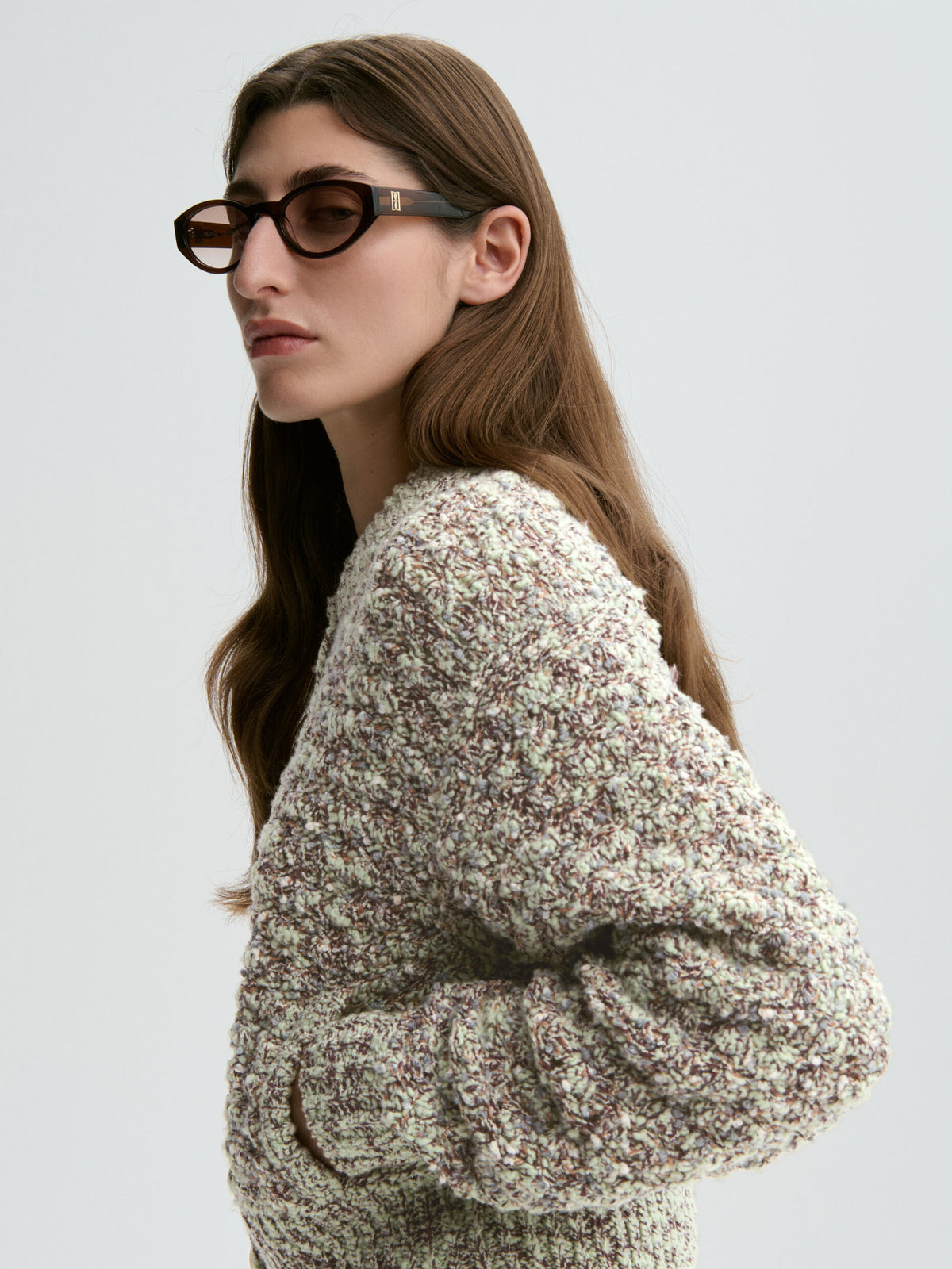 Woman wearing a textured sweater and sunglasses on a light gray background