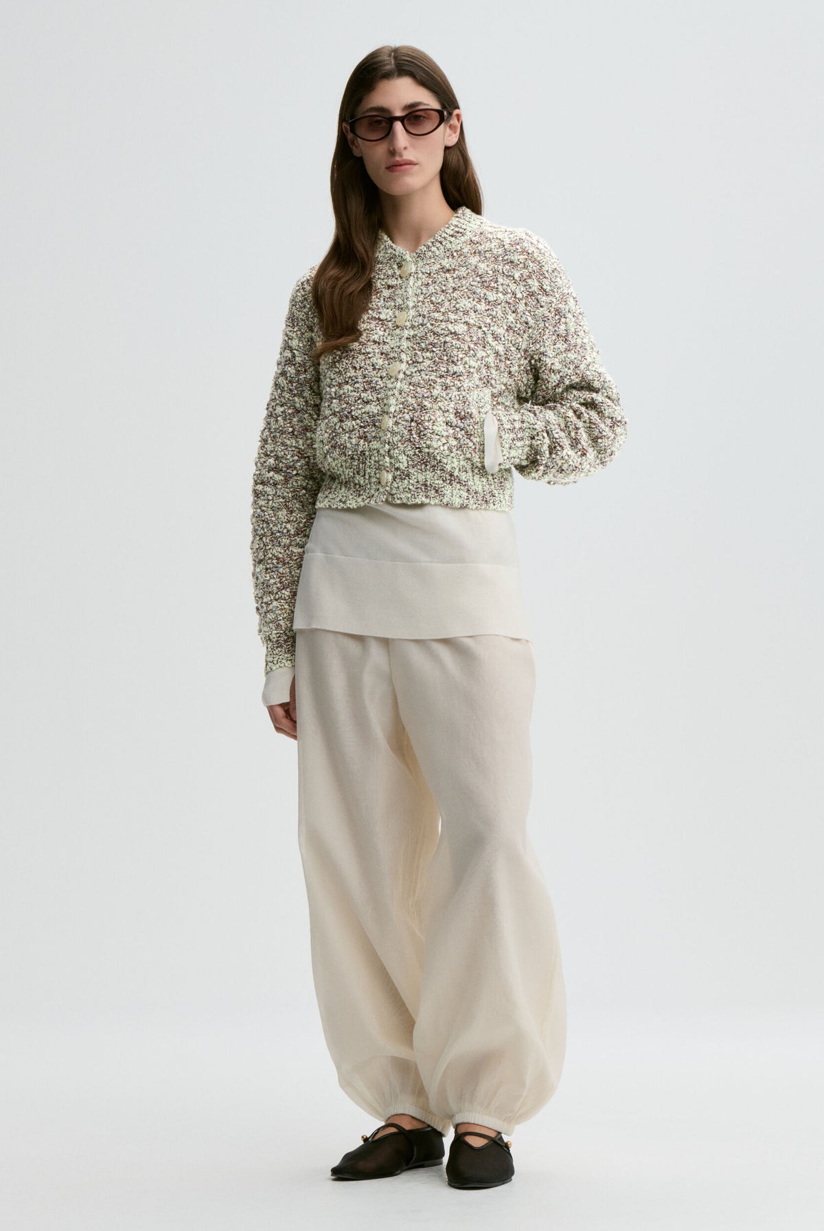 Person wearing a patterned sweater and beige pants on a white background