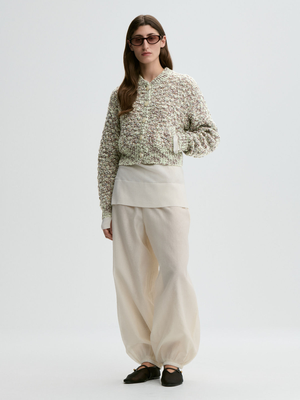 Person wearing a patterned sweater and beige pants on a white background