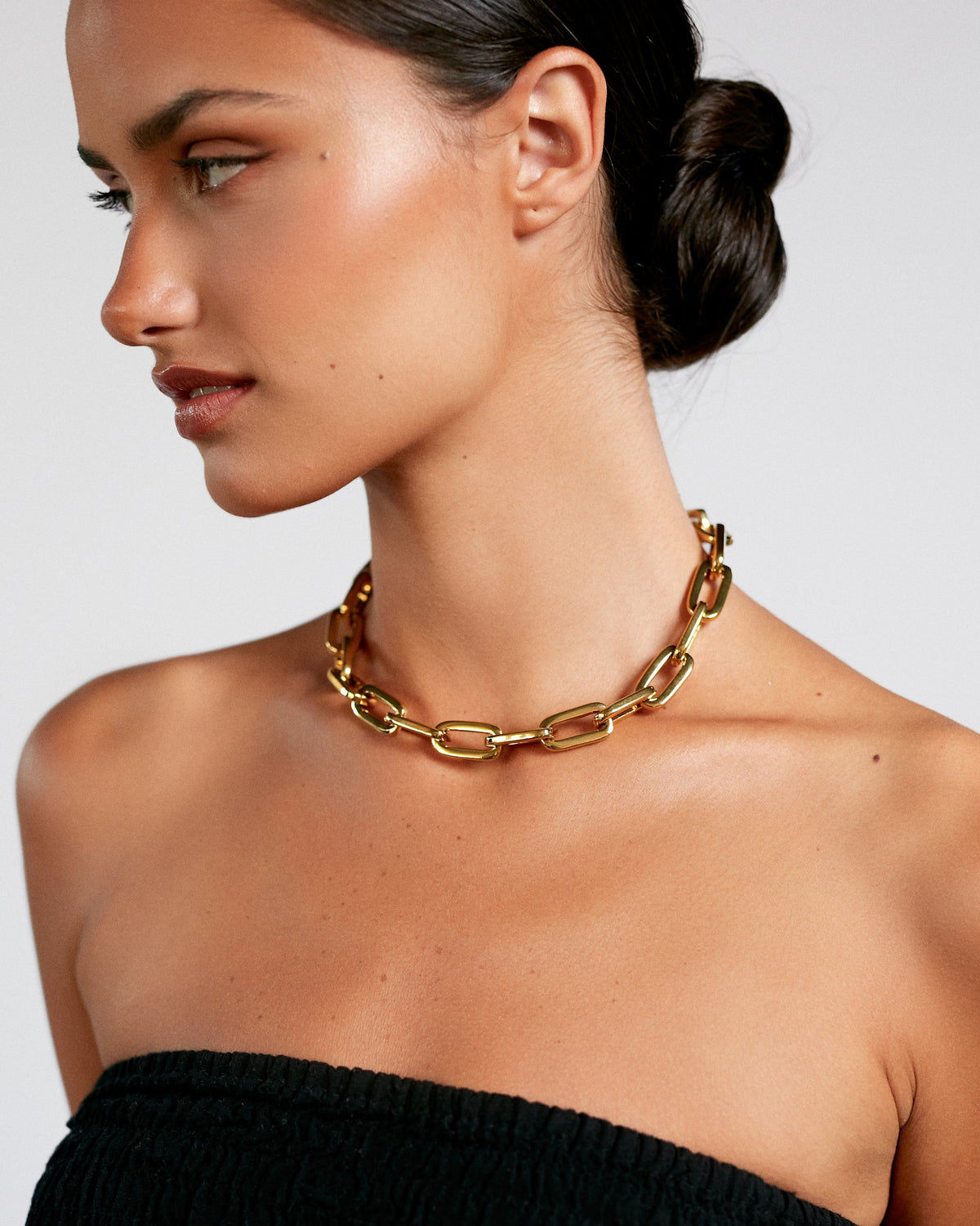 Woman wearing a gold chain necklace against a plain background