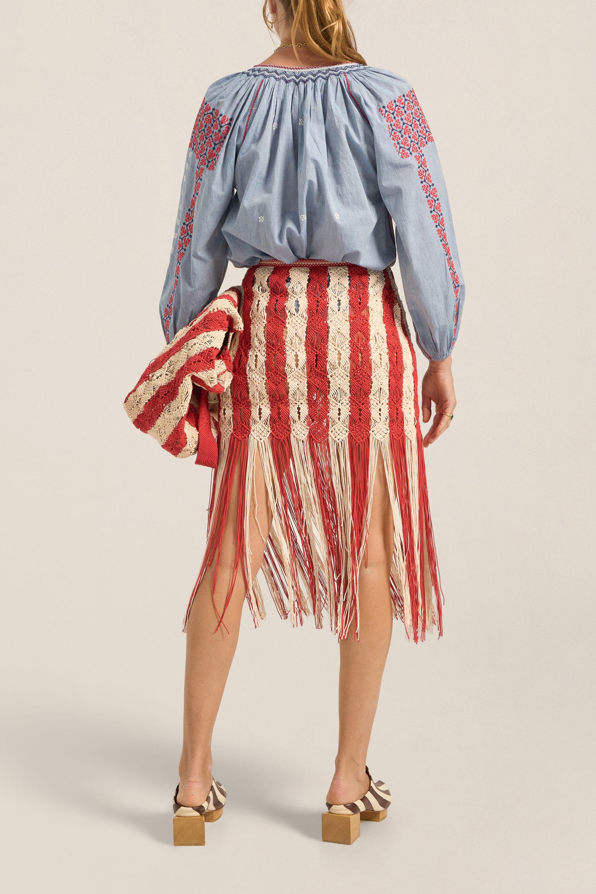 Woman wearing a blue embroidered blouse and red and white striped skirt on a beige background