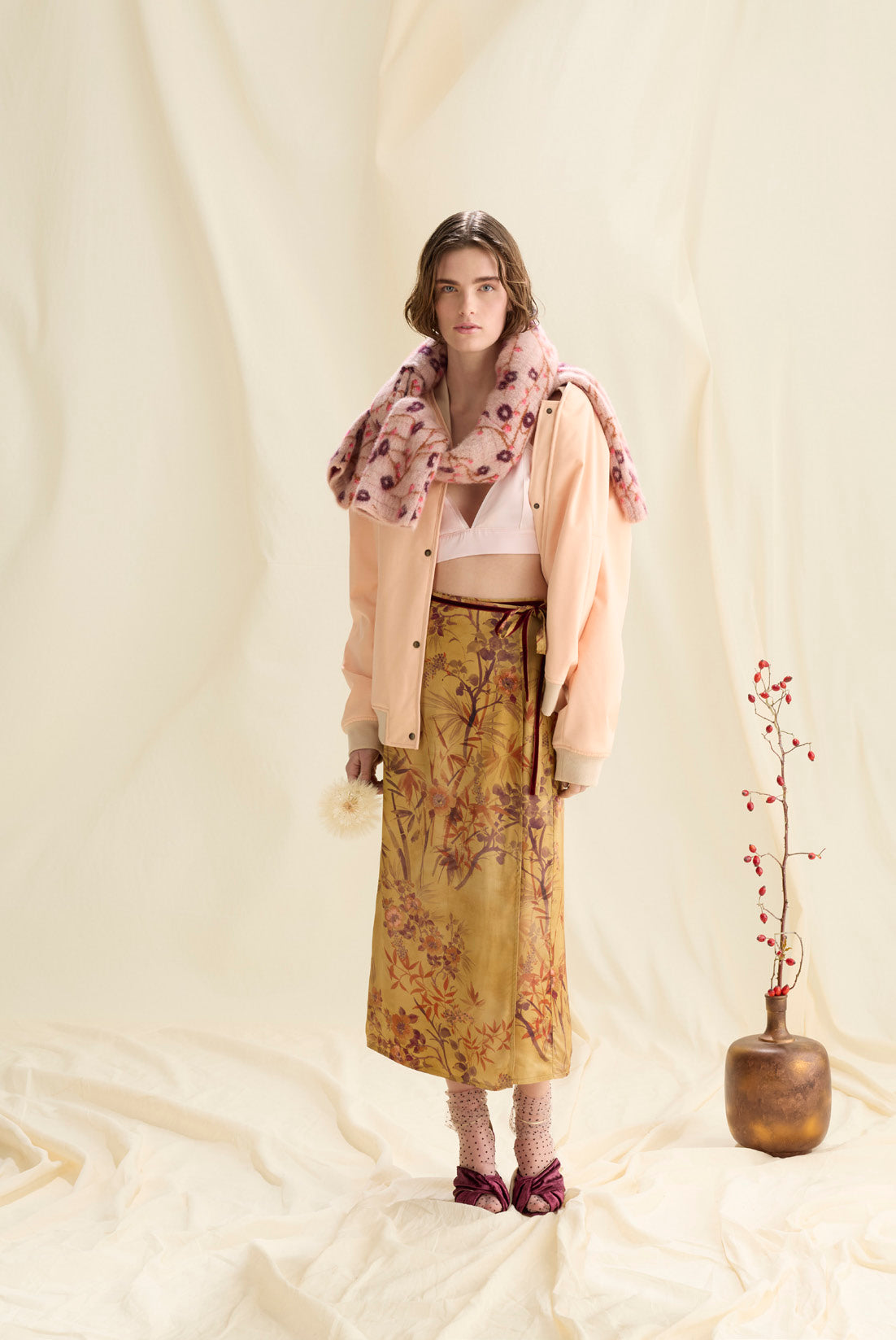 Woman wearing a floral outfit with a pink jacket and yellow skirt, standing against a white background.