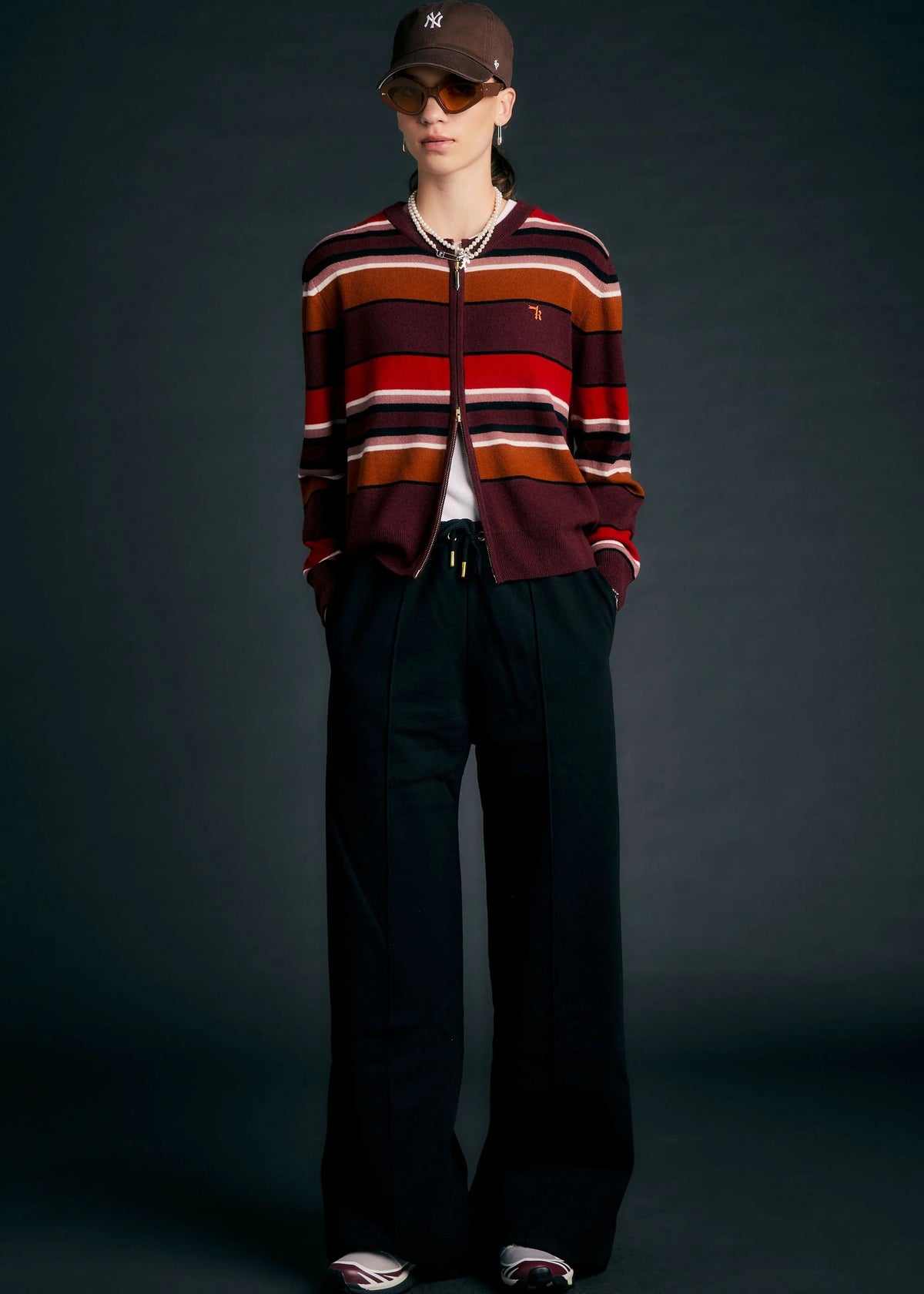 Person wearing a striped cardigan and dark pants against a dark background