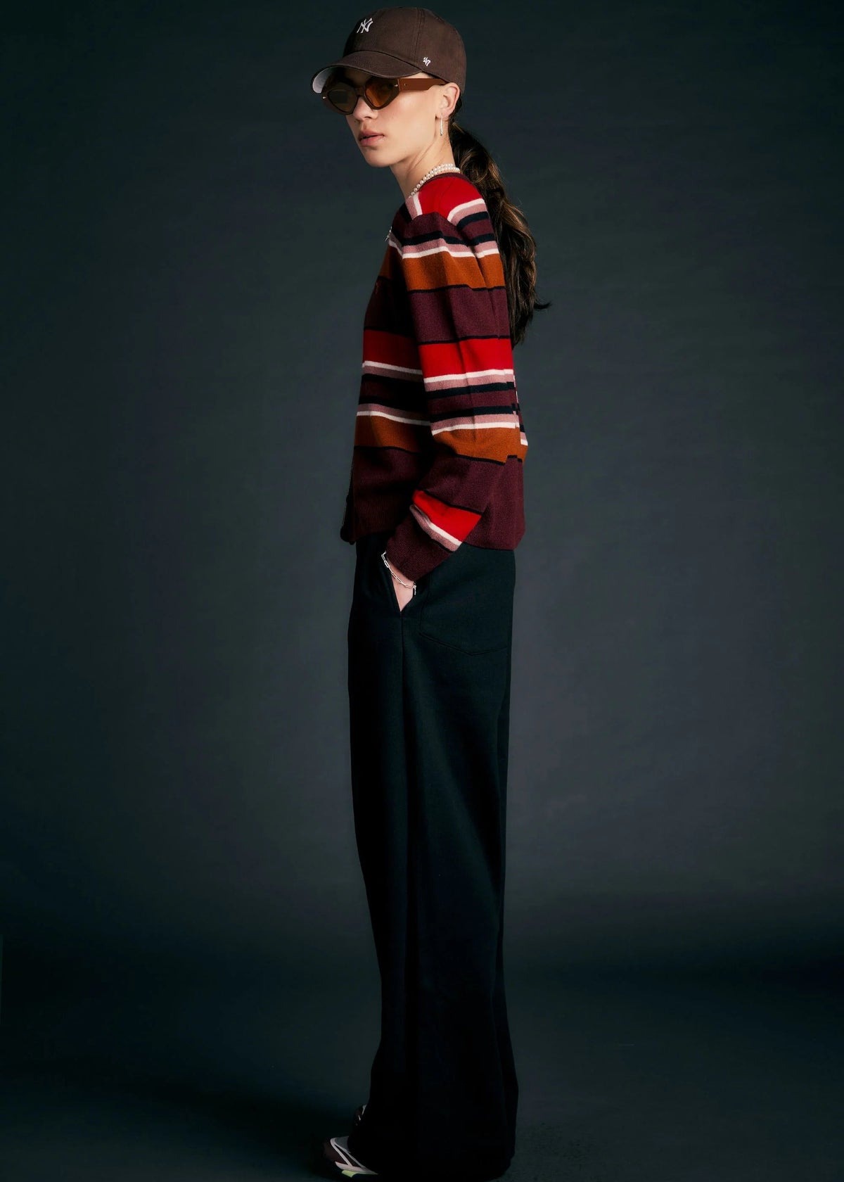Person wearing a striped sweater and dark pants against a dark background