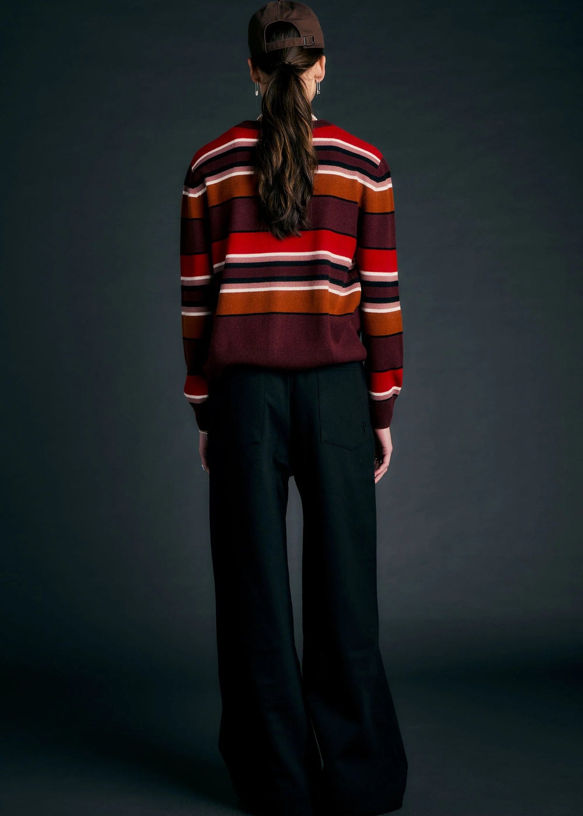 Person wearing a striped sweater and dark pants against a dark background