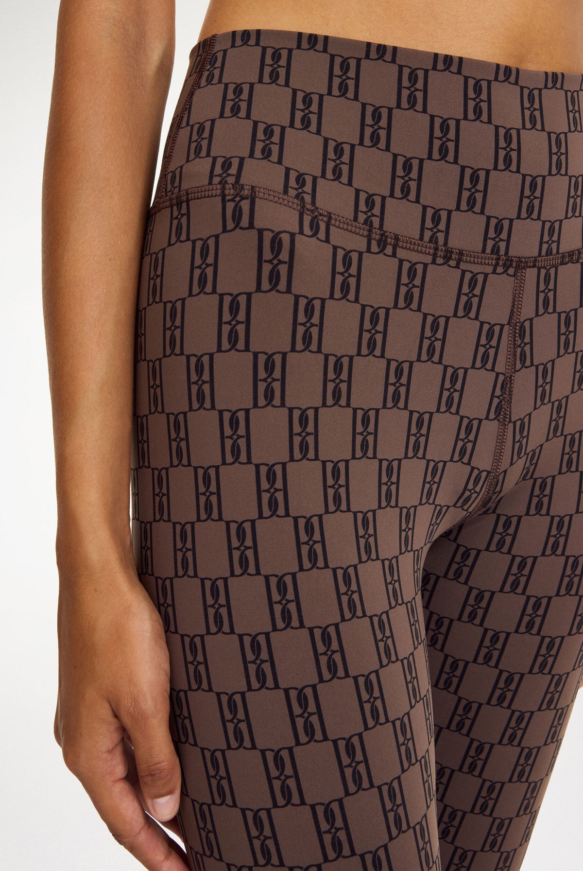 Brown leggings with a black geometric pattern worn by a person on a white background