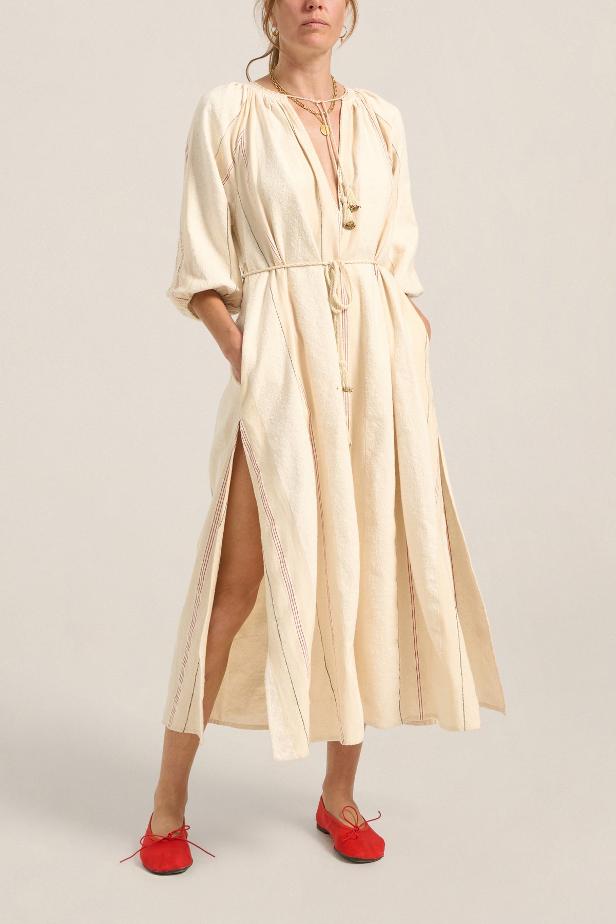 Woman wearing a beige dress with a slit on a plain background