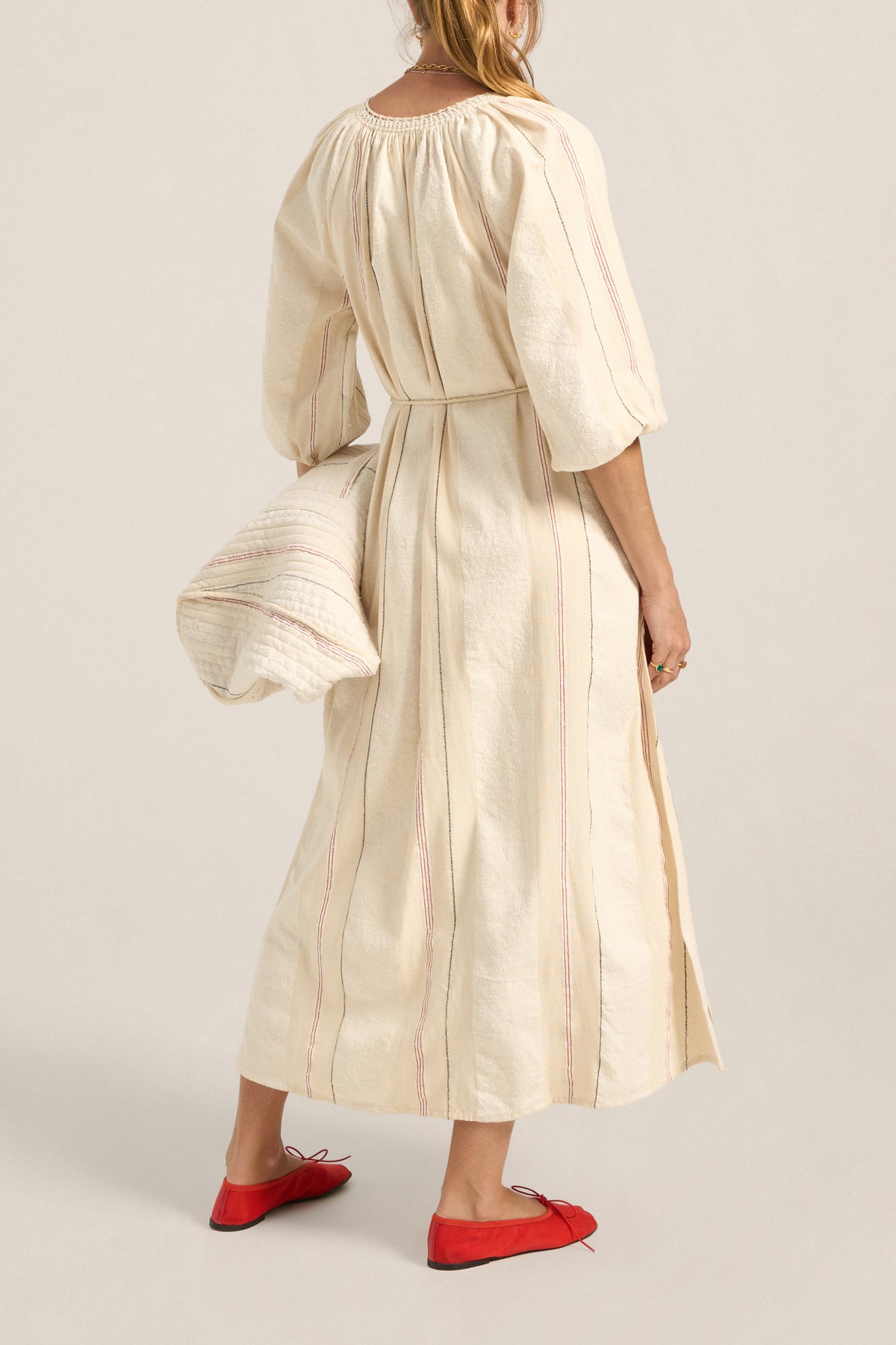 Woman wearing a beige dress with a belt, standing against a plain background