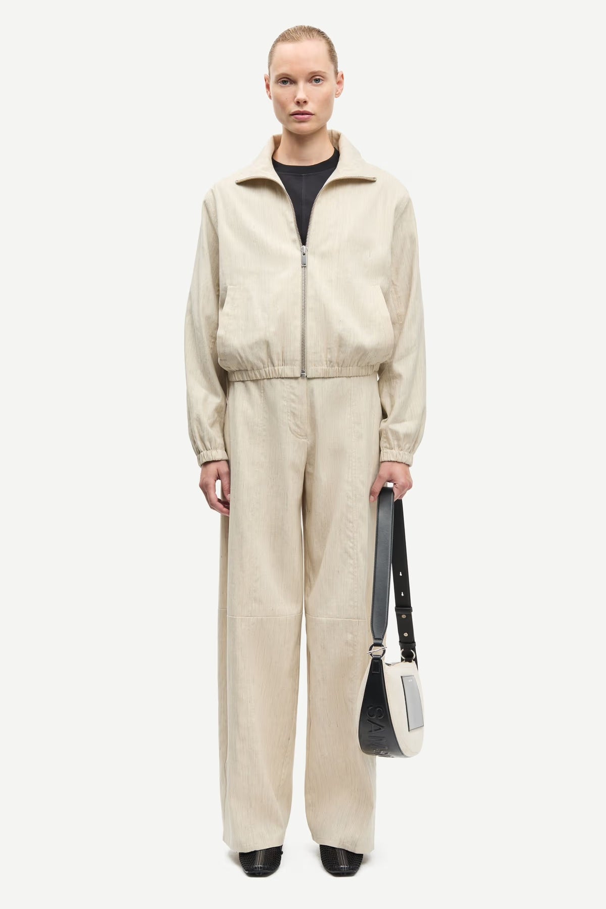 Person wearing a beige tracksuit holding a black bag on a white background
