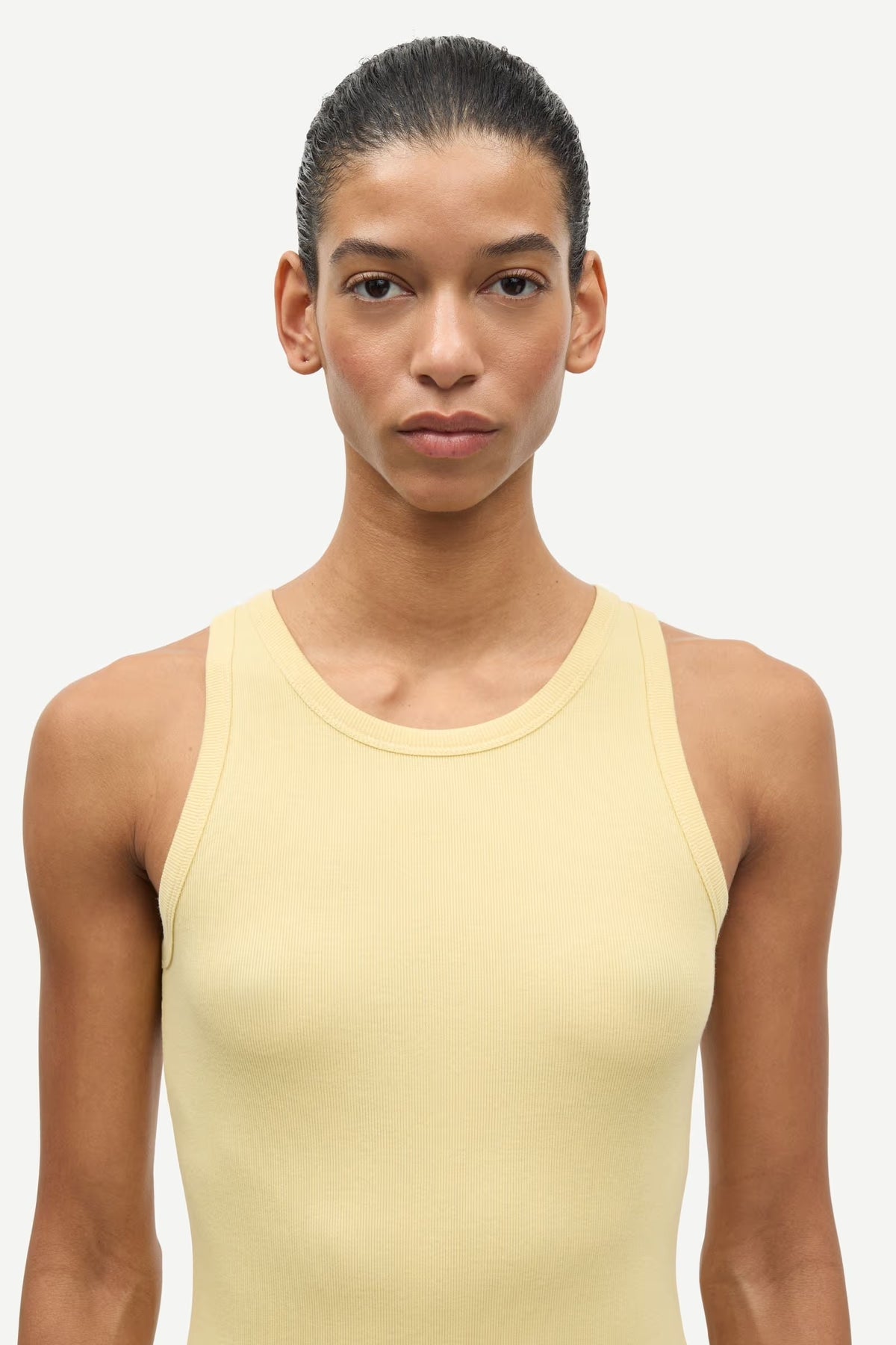 Woman wearing a light yellow tank top against a white background
