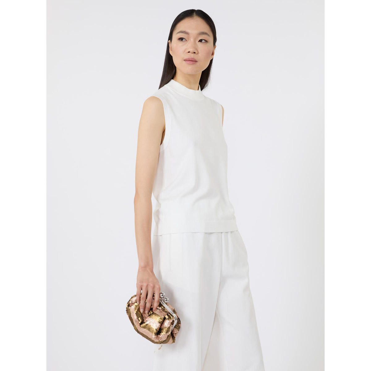 Woman in a white outfit holding a gold clutch against a white background