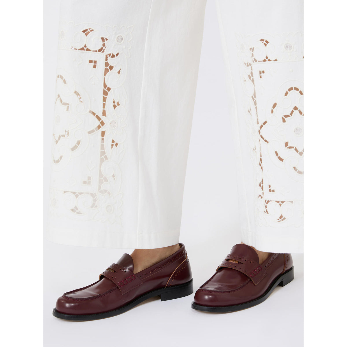 Brown loafers worn with white pants featuring floral embroidery on a white background