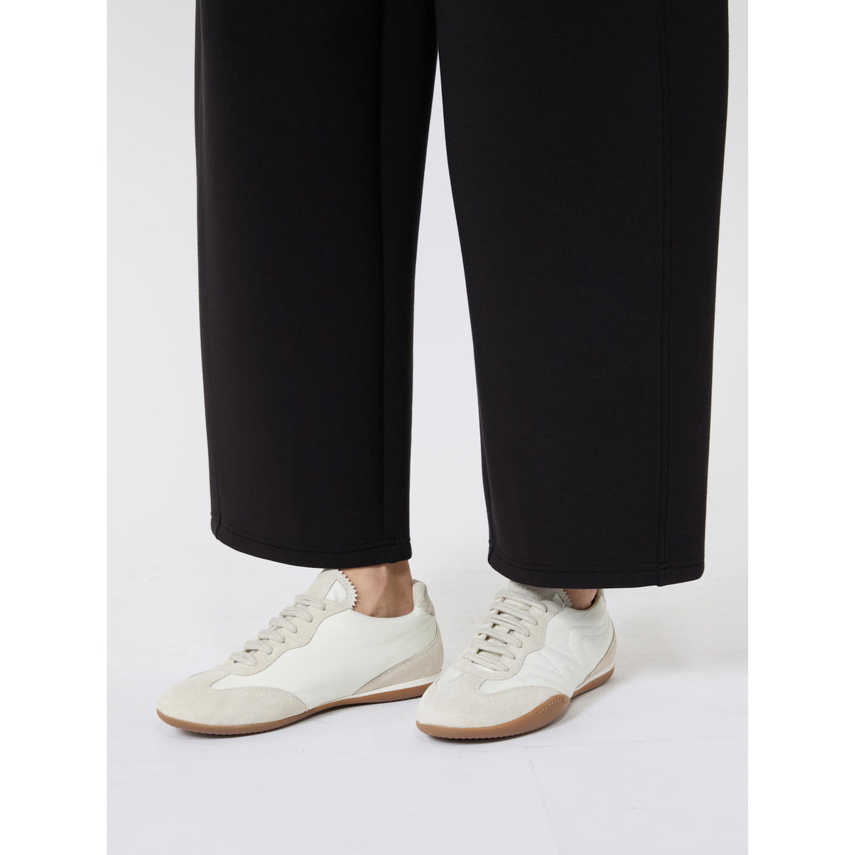 White sneakers worn with black pants on a white background