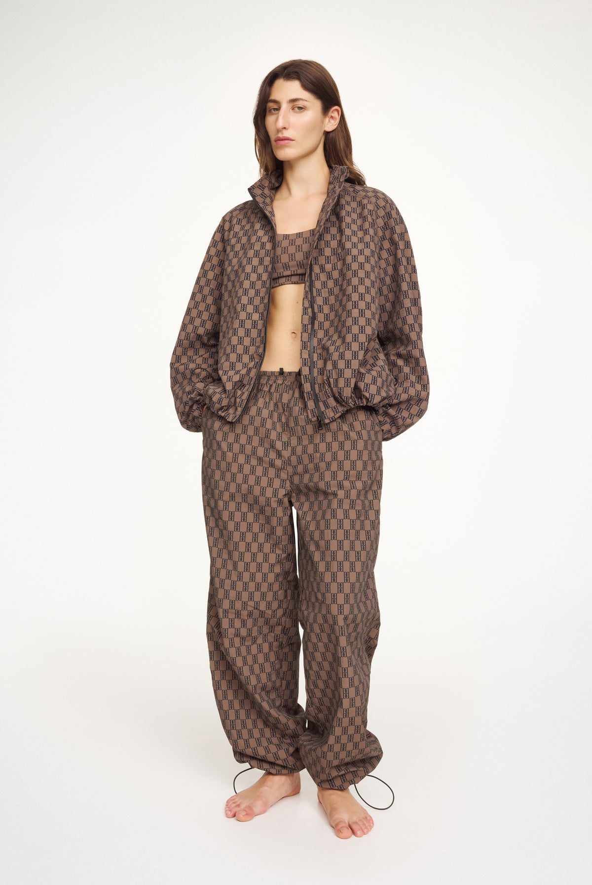 Person wearing a brown patterned anorak, bra and pants by Malene Birger on a white background