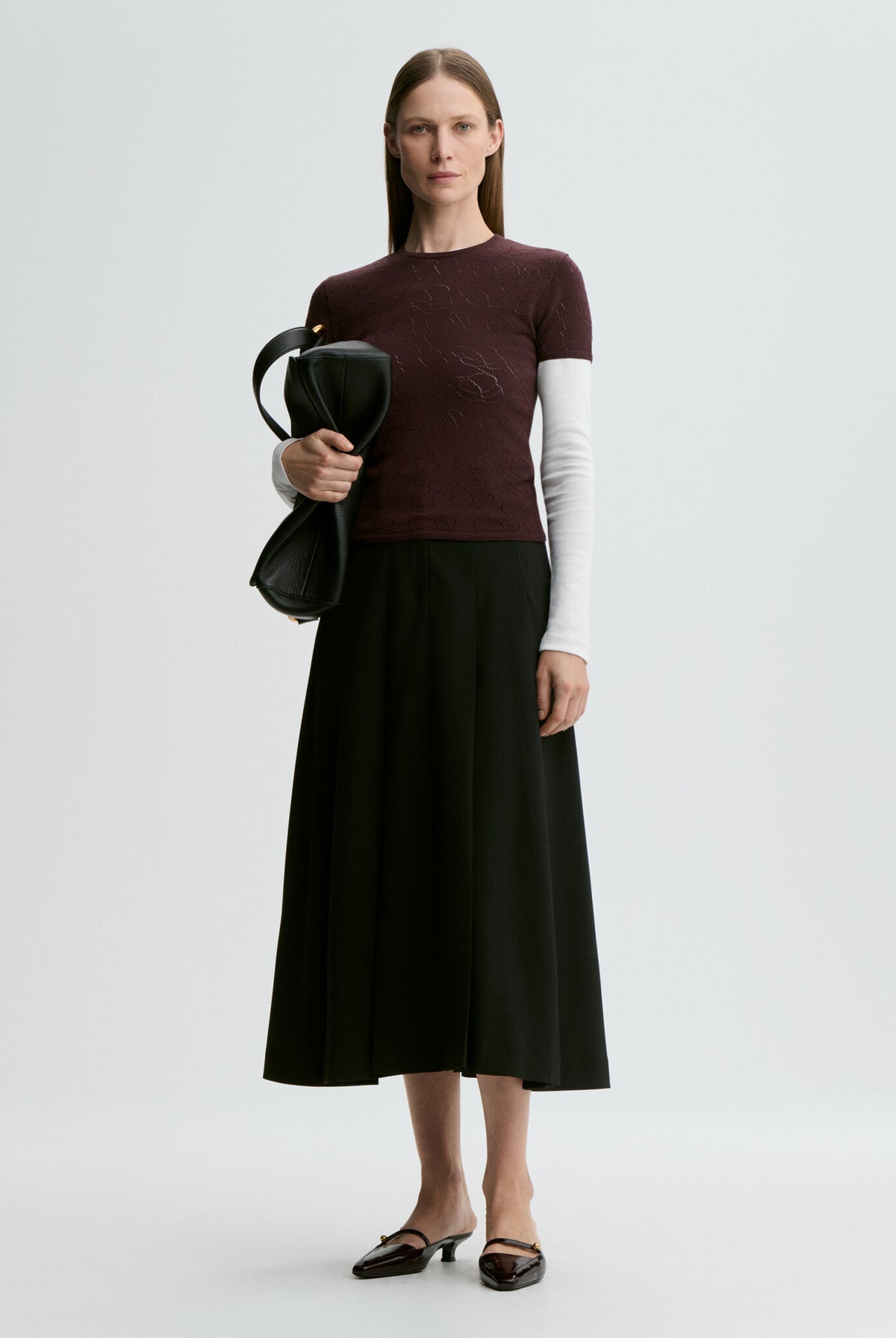 Woman wearing a maroon sweater and black skirt holding a black bag on a white background