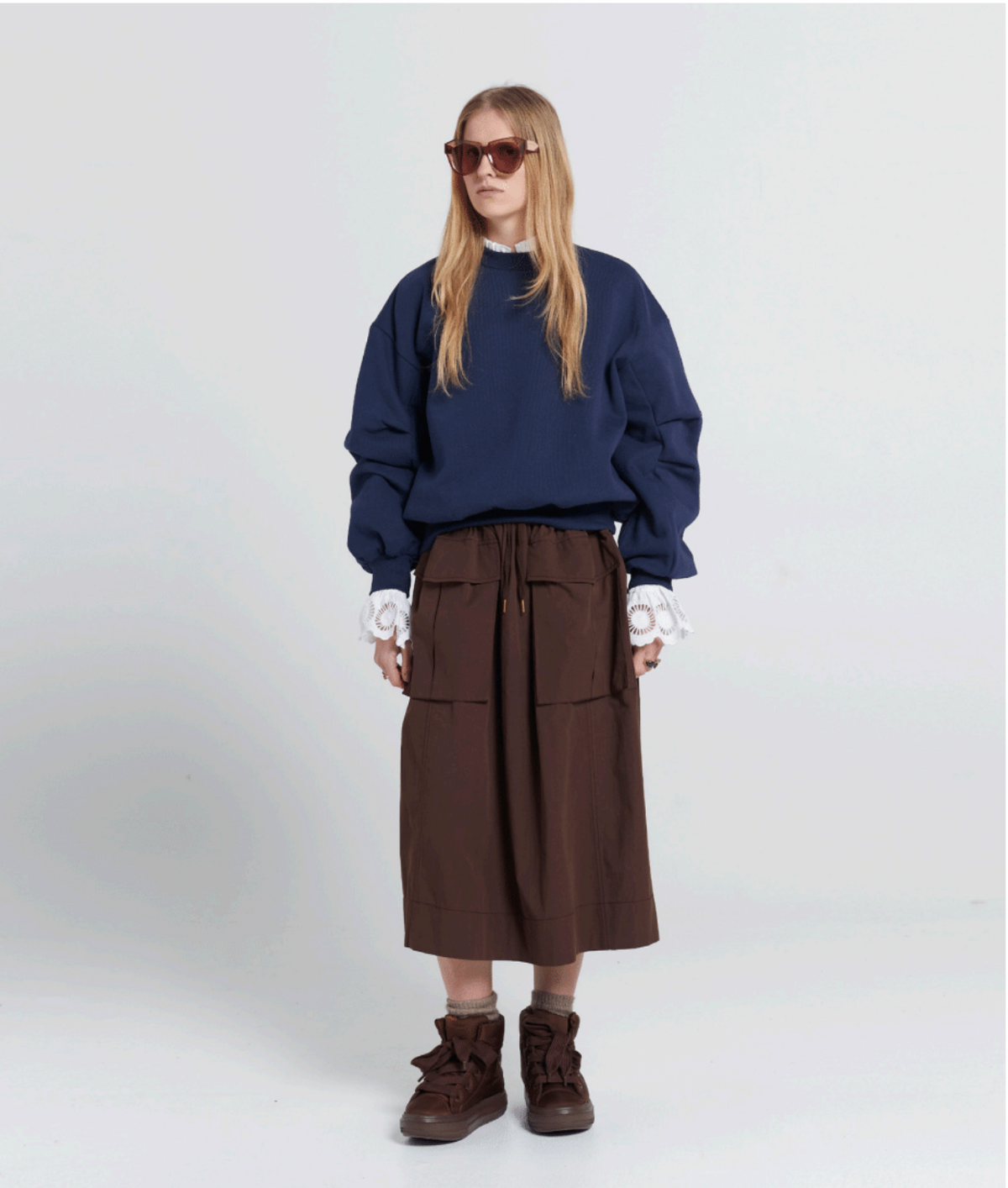 Person wearing a navy sweater and brown skirt on a white background