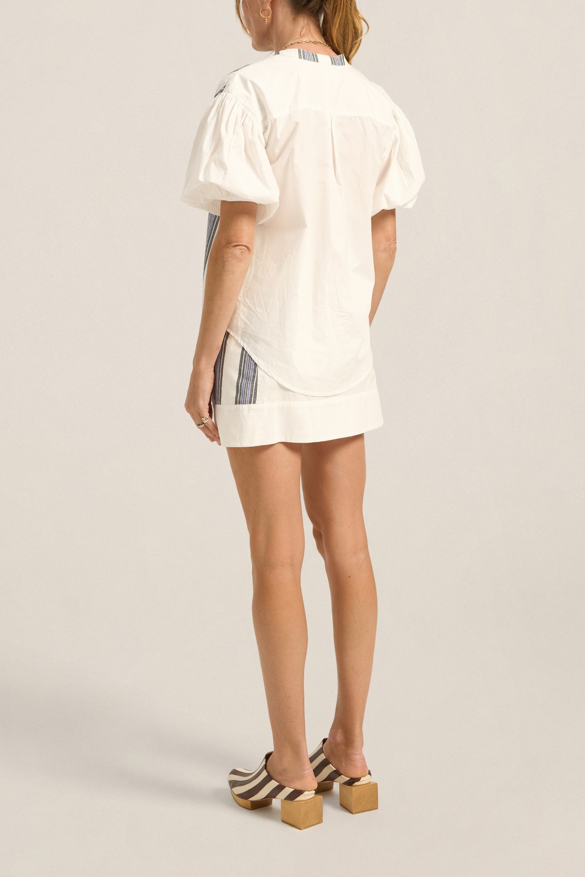 Person wearing a white outfit with a plaid skirt on a plain background