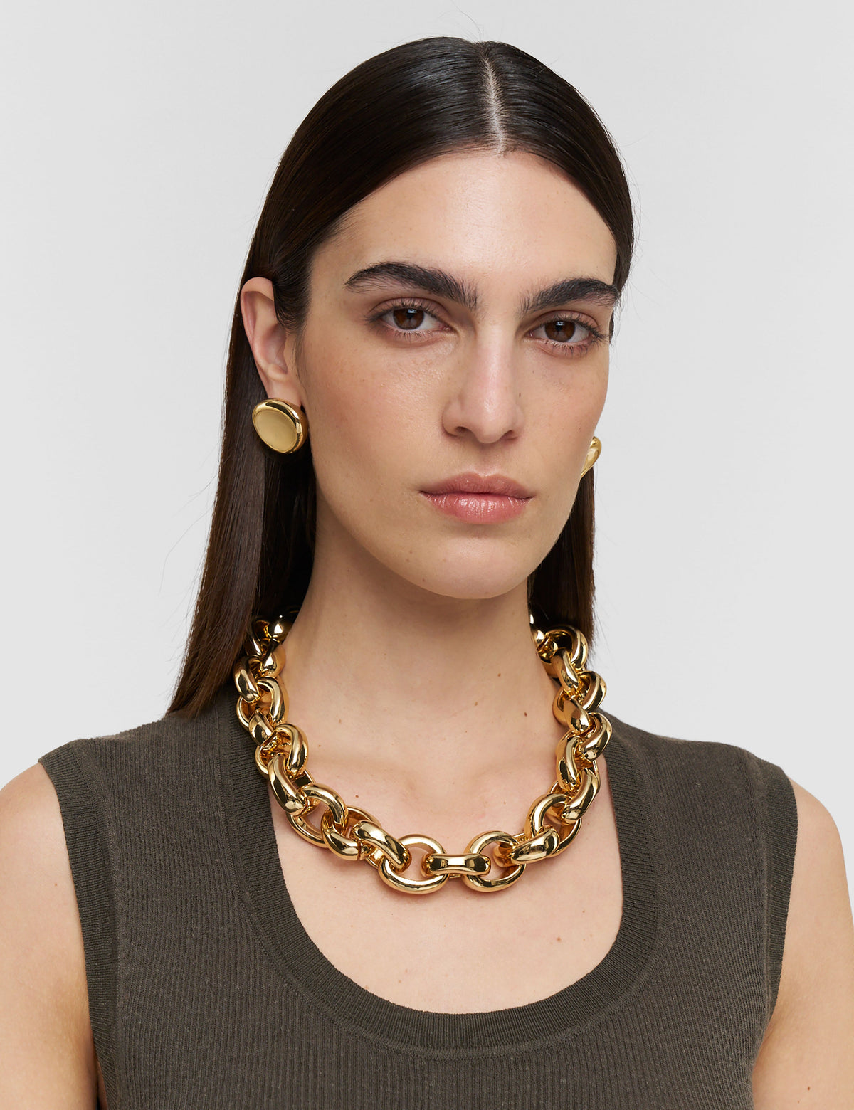 Woman wearing a gold chain necklace and earrings on a plain background