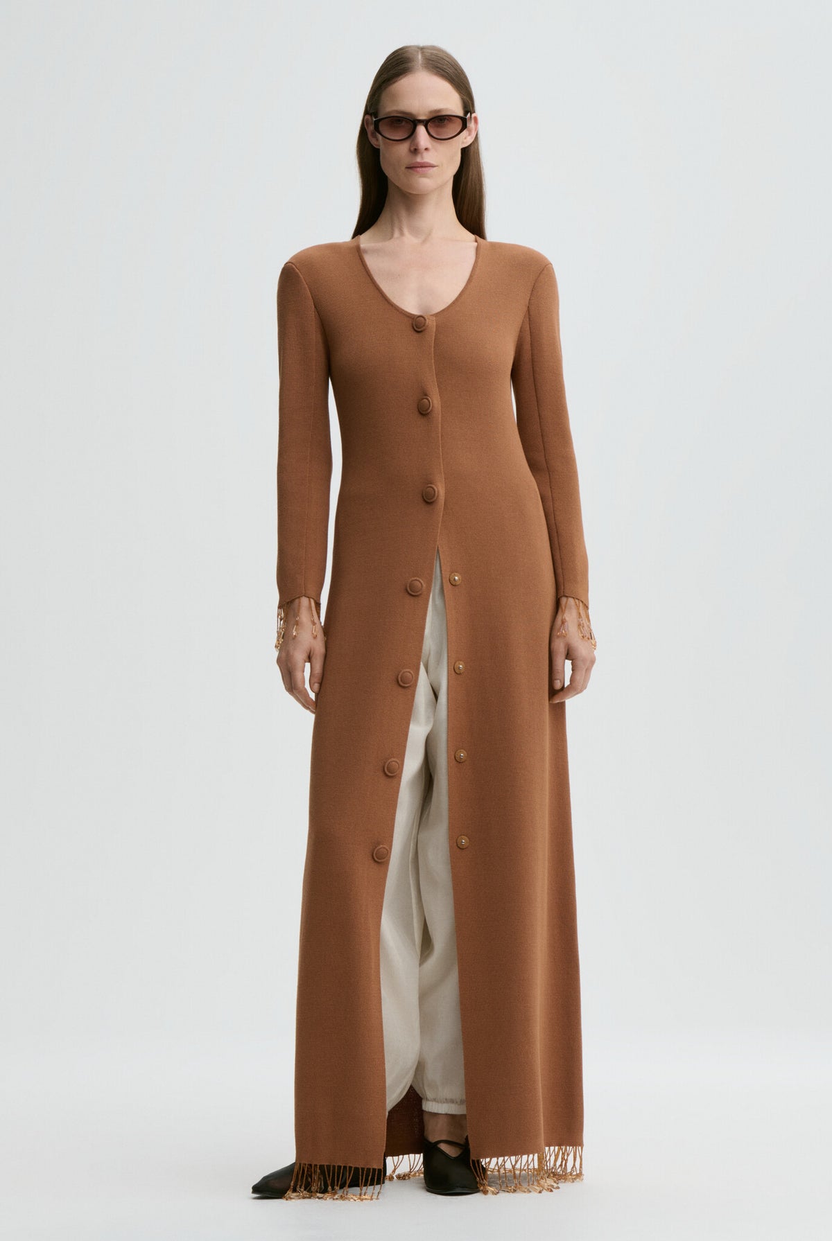 Woman wearing a long brown cardigan over a white dress on a light gray background