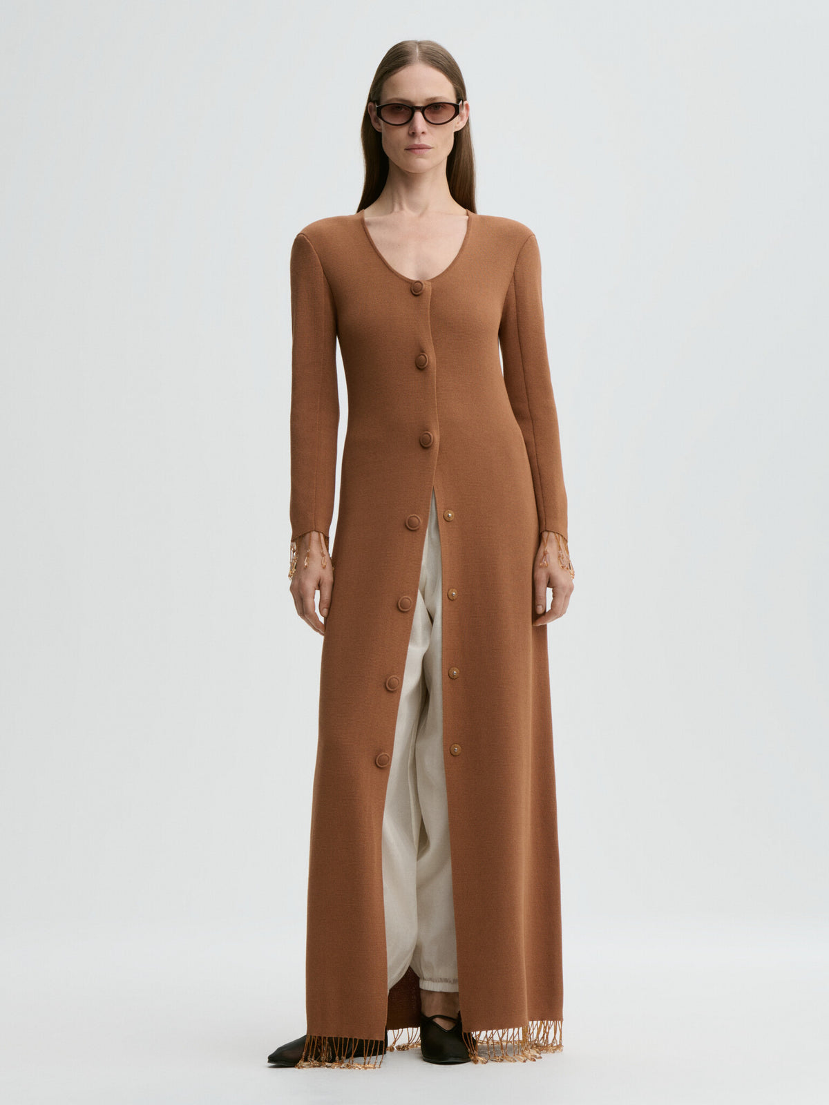 Woman wearing a long brown cardigan over a white dress on a light gray background