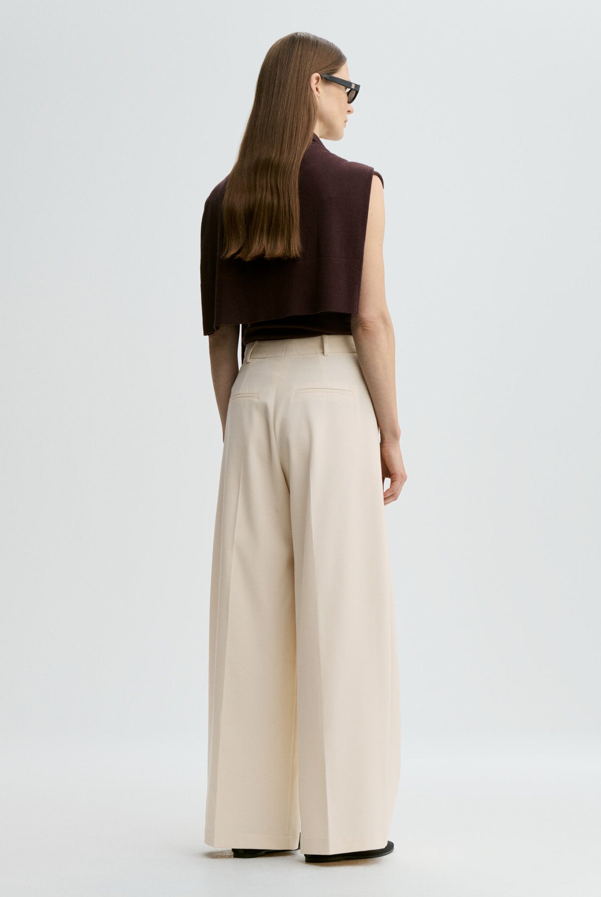 Woman wearing a brown top and beige wide-leg pants on a white background