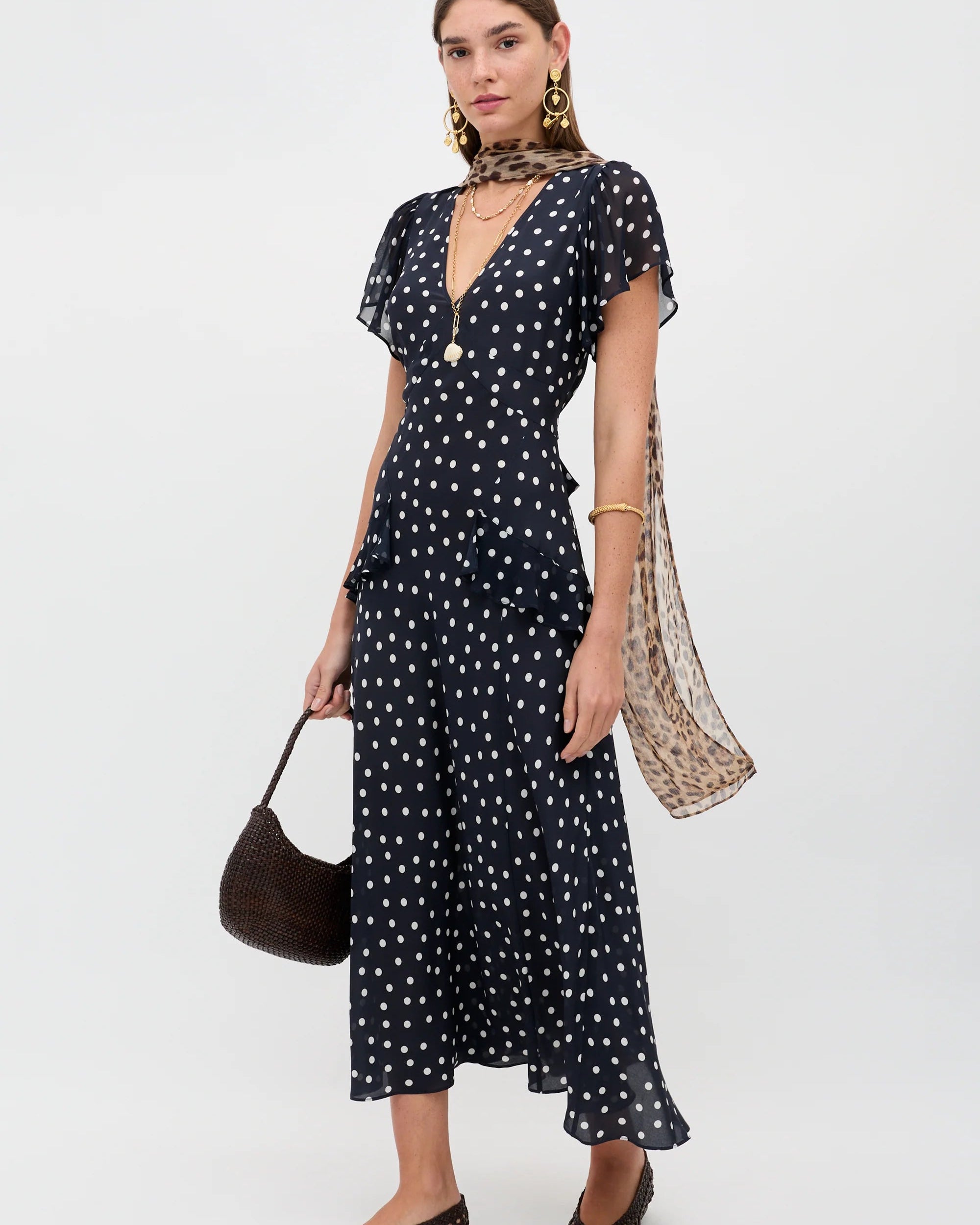 Woman wearing a black dress with white polka dots, holding a patterned scarf and bag on a white background
