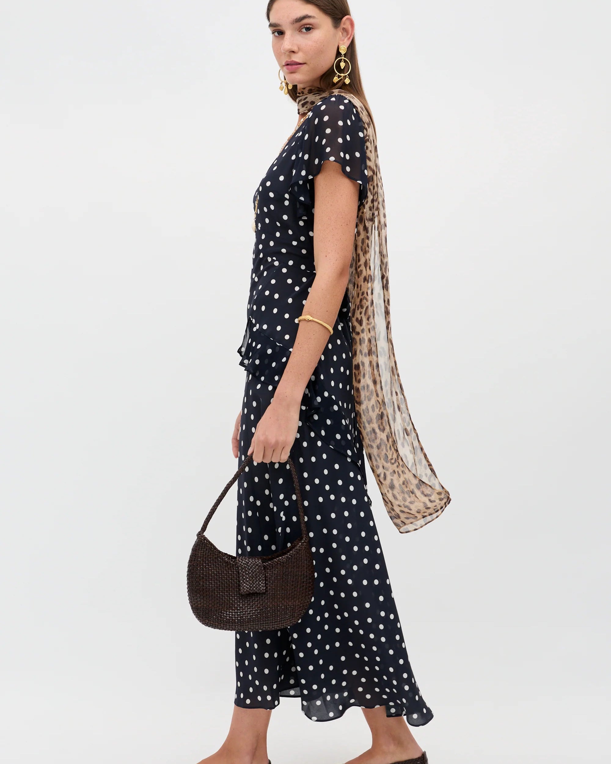 Woman wearing a black polka dot dress with a long scarf and holding a handbag on a white background