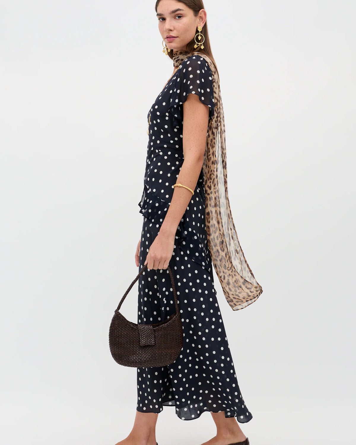 Woman wearing a black polka dot dress with a long scarf and holding a handbag on a white background
