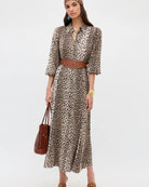 Woman wearing a leopard print dress with a brown belt and holding a brown bag on a white background