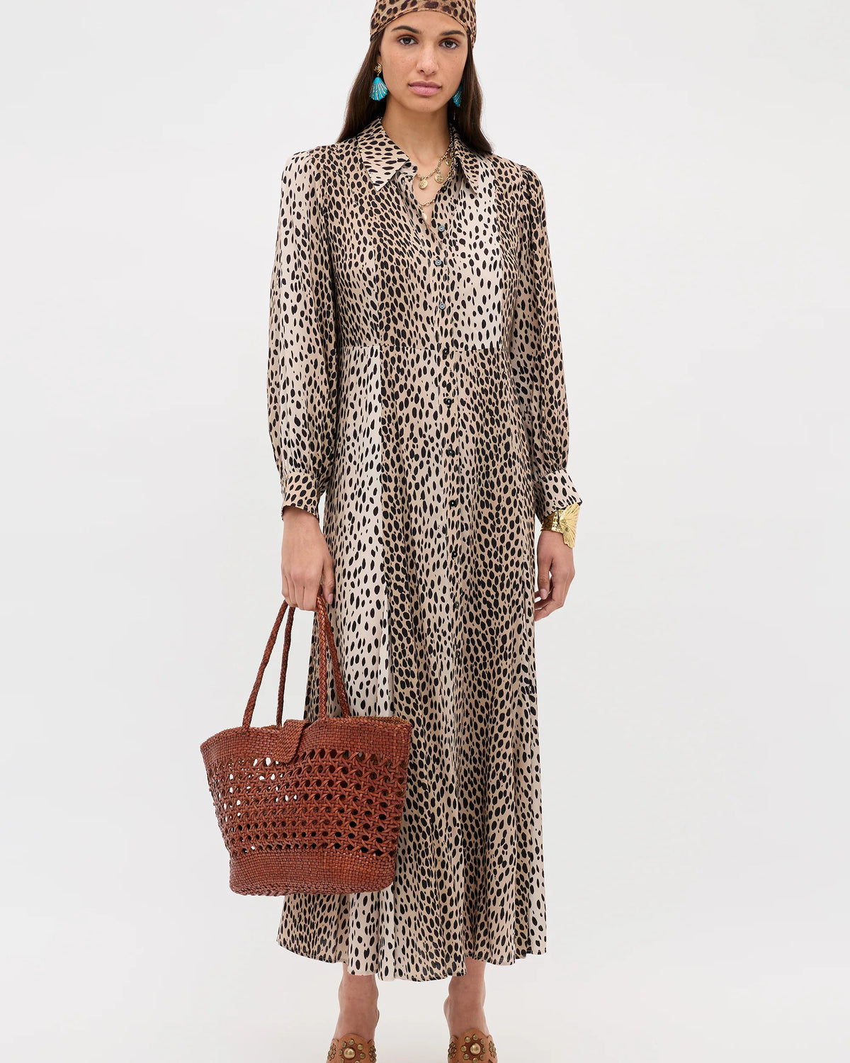 Woman wearing a leopard print dress holding a brown woven bag on a white background