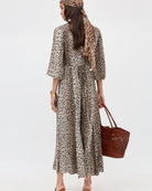 Woman wearing a leopard print dress and headscarf, holding a brown bag on a white background