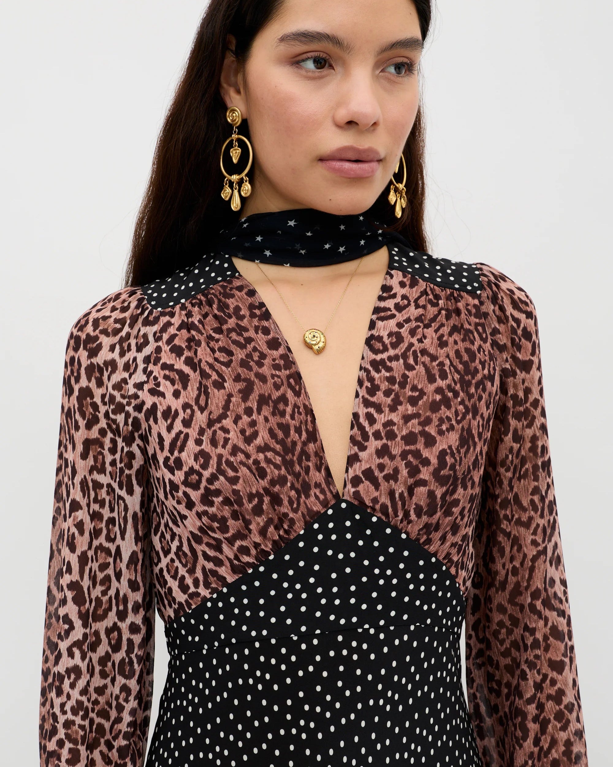 Woman wearing a leopard print top over a black polka dot dress on a white background