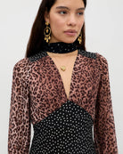 Woman wearing a leopard print top over a black polka dot dress on a white background