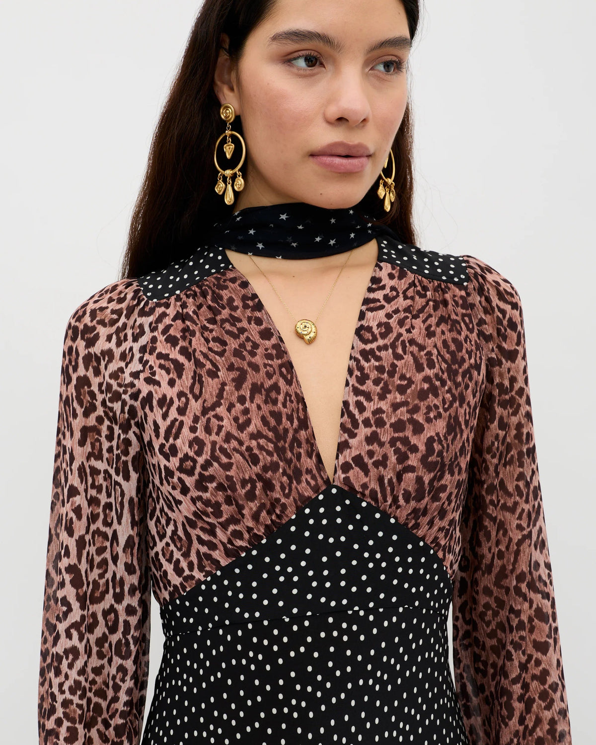 Woman wearing a leopard print top over a black polka dot dress on a white background