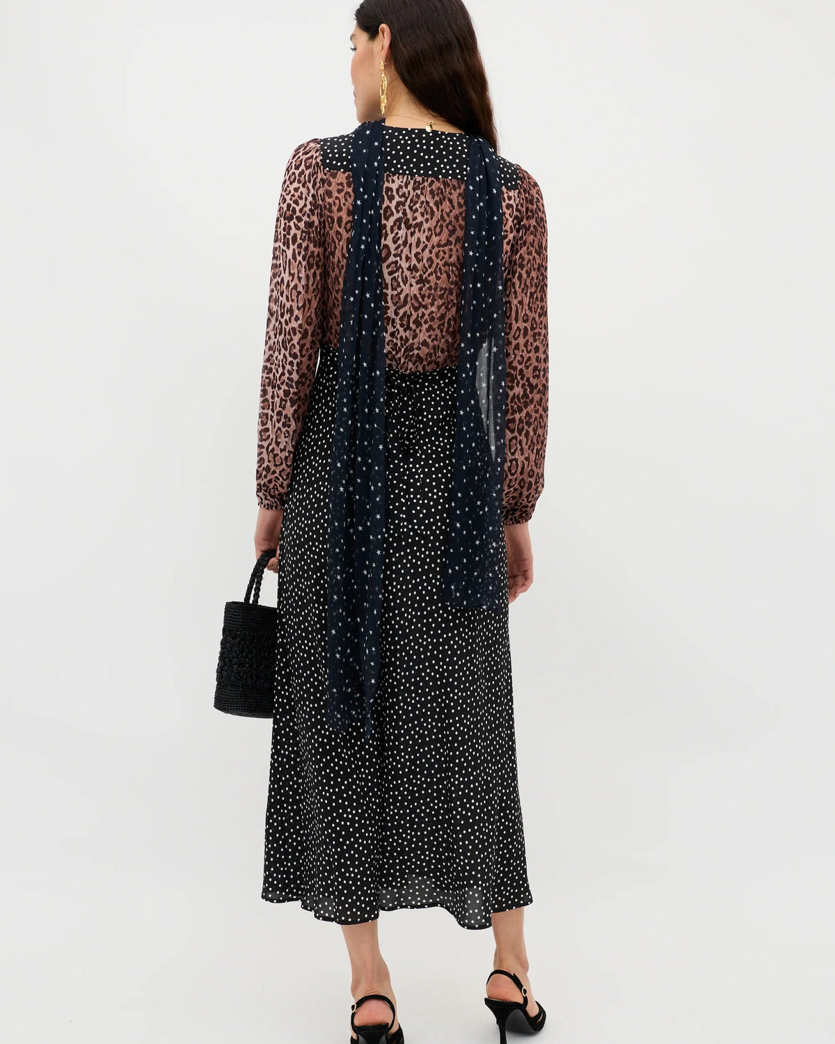 Woman wearing a black polka dot dress with a sheer overlay on a white background