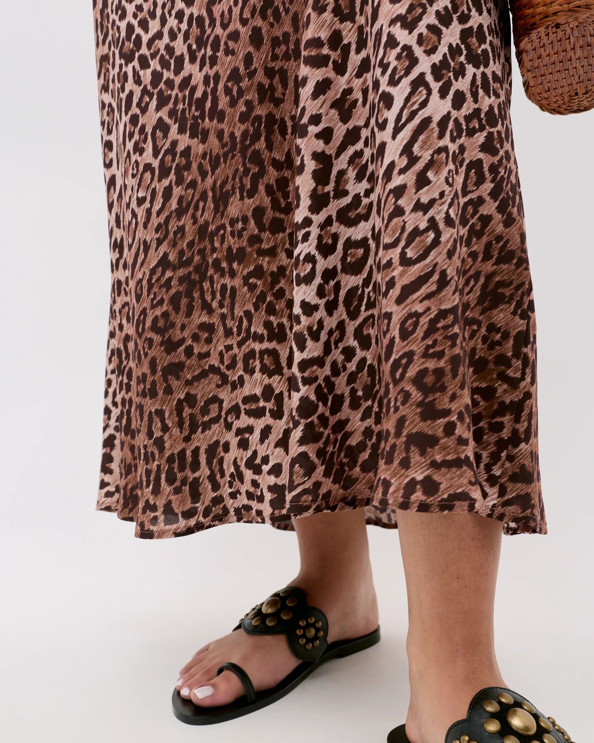 Person wearing a leopard print dress and black sandals on a white background