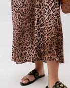 Person wearing a leopard print dress and black sandals on a white background