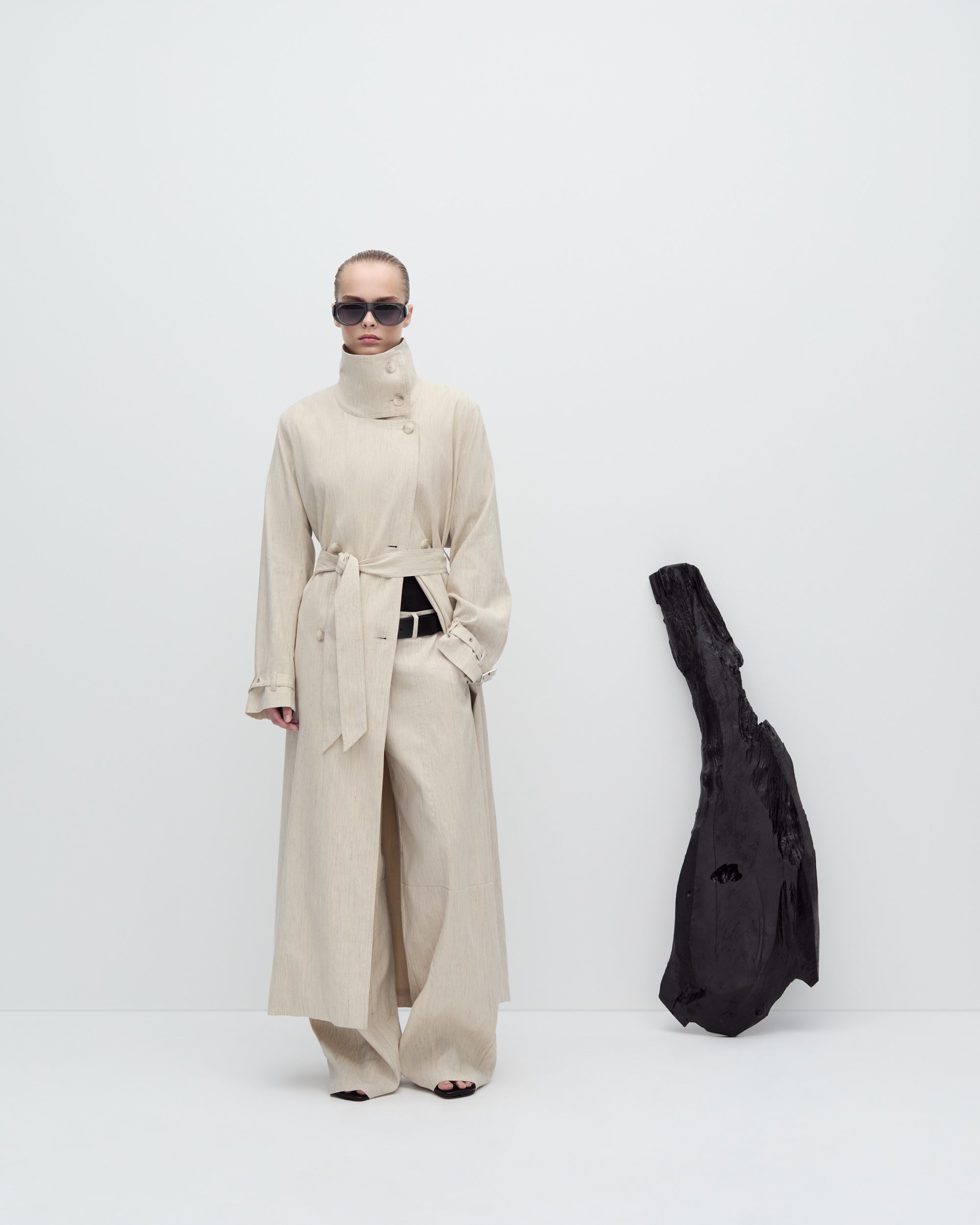 Person wearing a long beige coat with a black bag on a white background