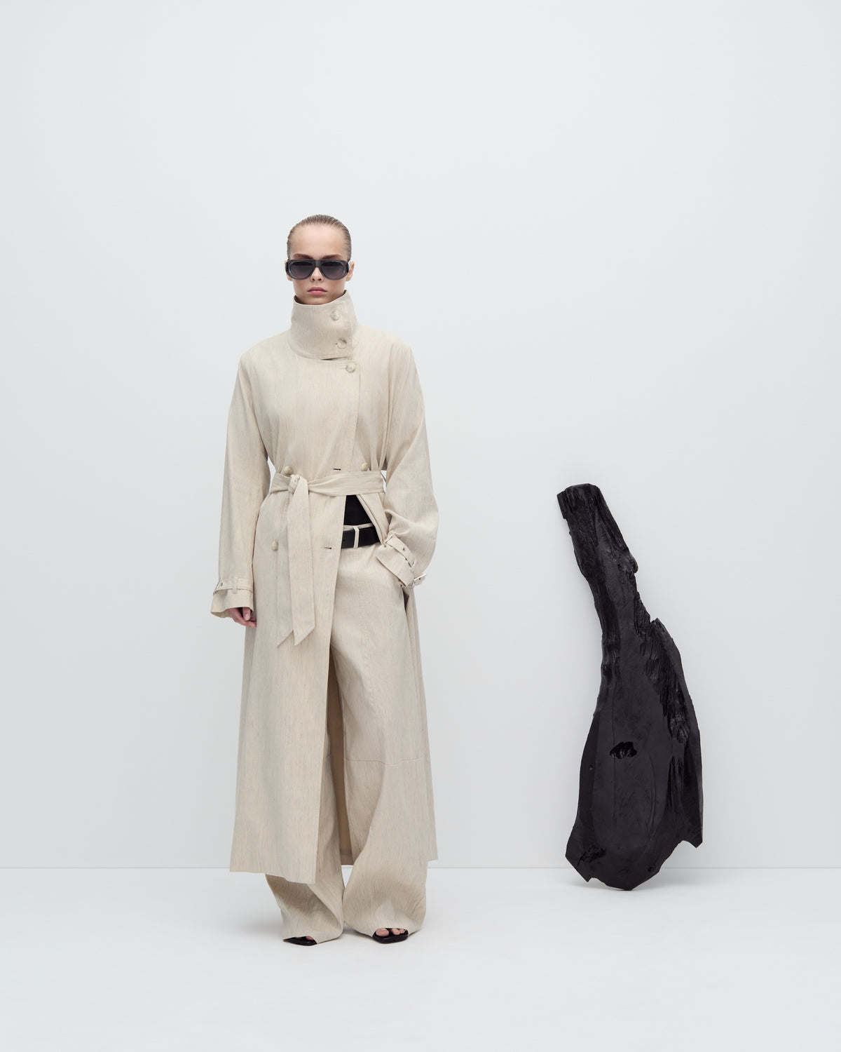 Person wearing a long beige coat with a black bag on a white background